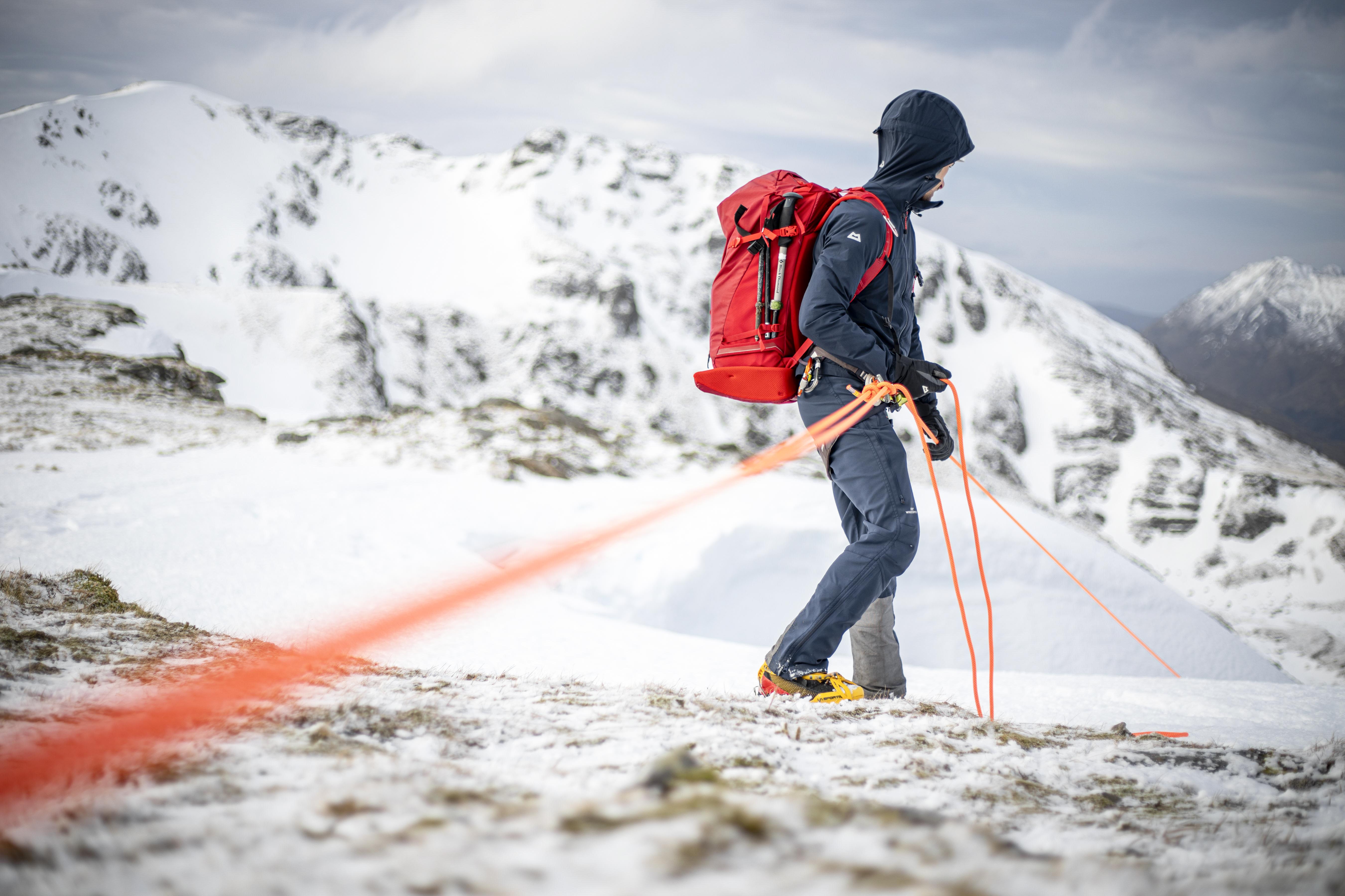 Image shows Mountain Rescue Team walking with the aid of orange rope on a snowy mountain.