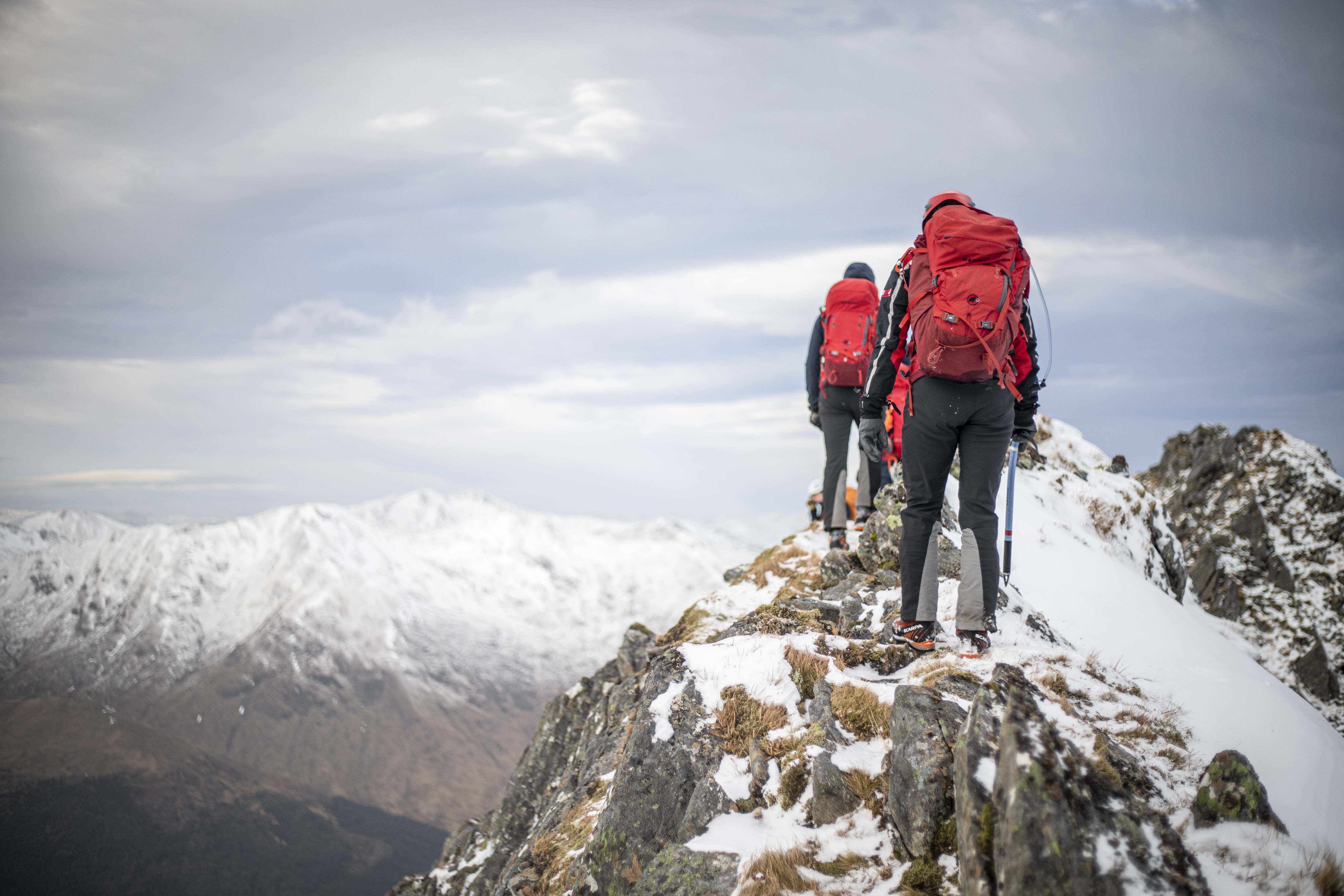Image shows Mountain Rescue Team walking along the top of a snowy mountain ridge.