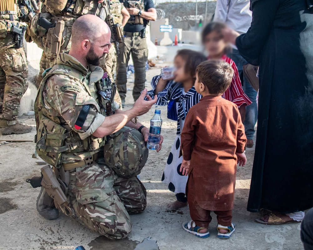 Personnel offers Afghan children water bottles.