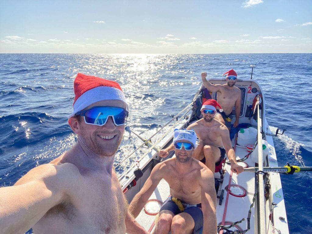 Rowers wearing Santa hats on the ocean.