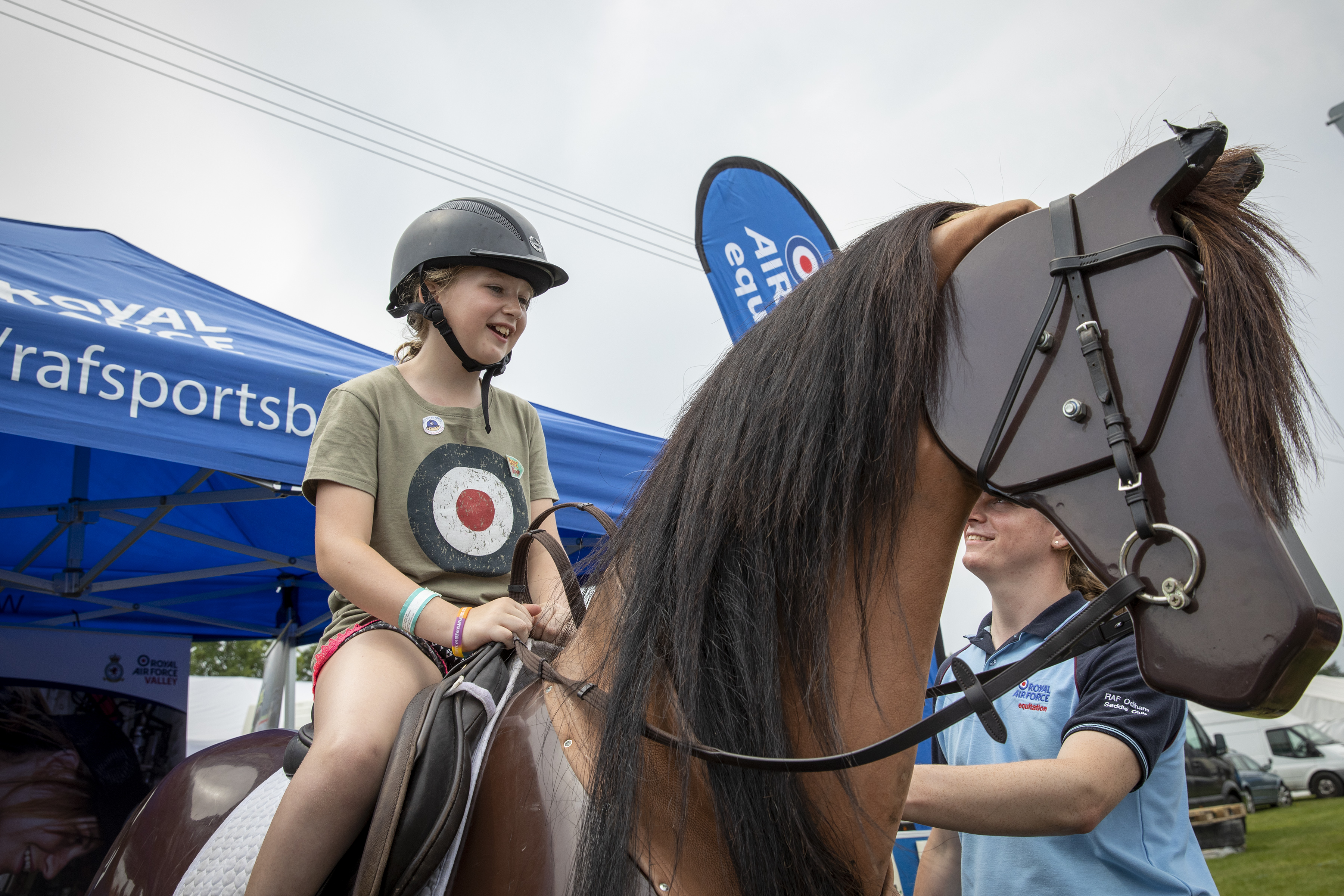 Image shows child in the seat of a horse simulator, with RAF volunteer.