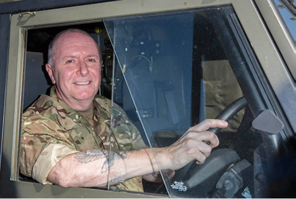 Reservists smiles behind driving wheel of truck vehicle.