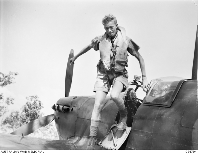 Black and white image of RAF pilot climbing out from a Spitfire on the airfield.