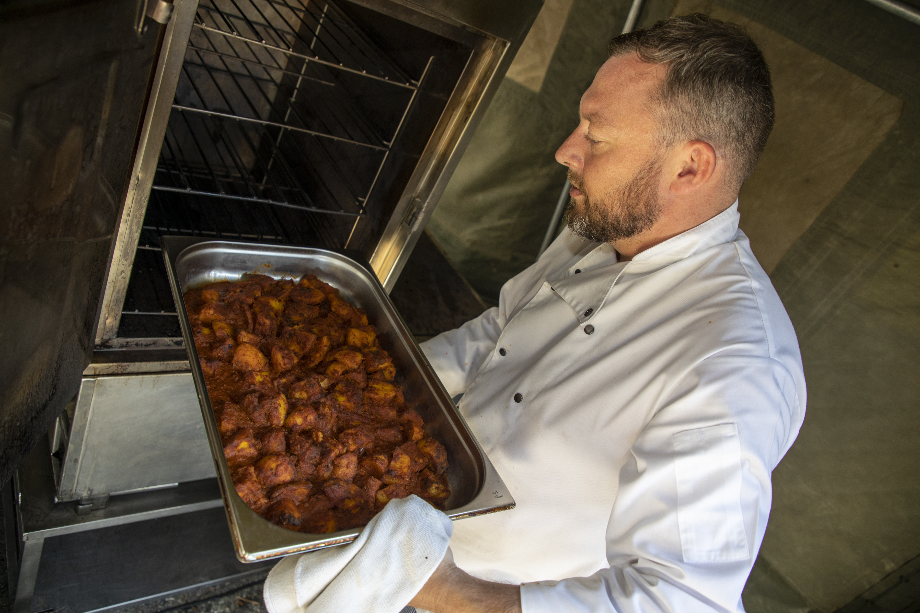 Image shows chef taking cooked potatoes out of industrial oven. 