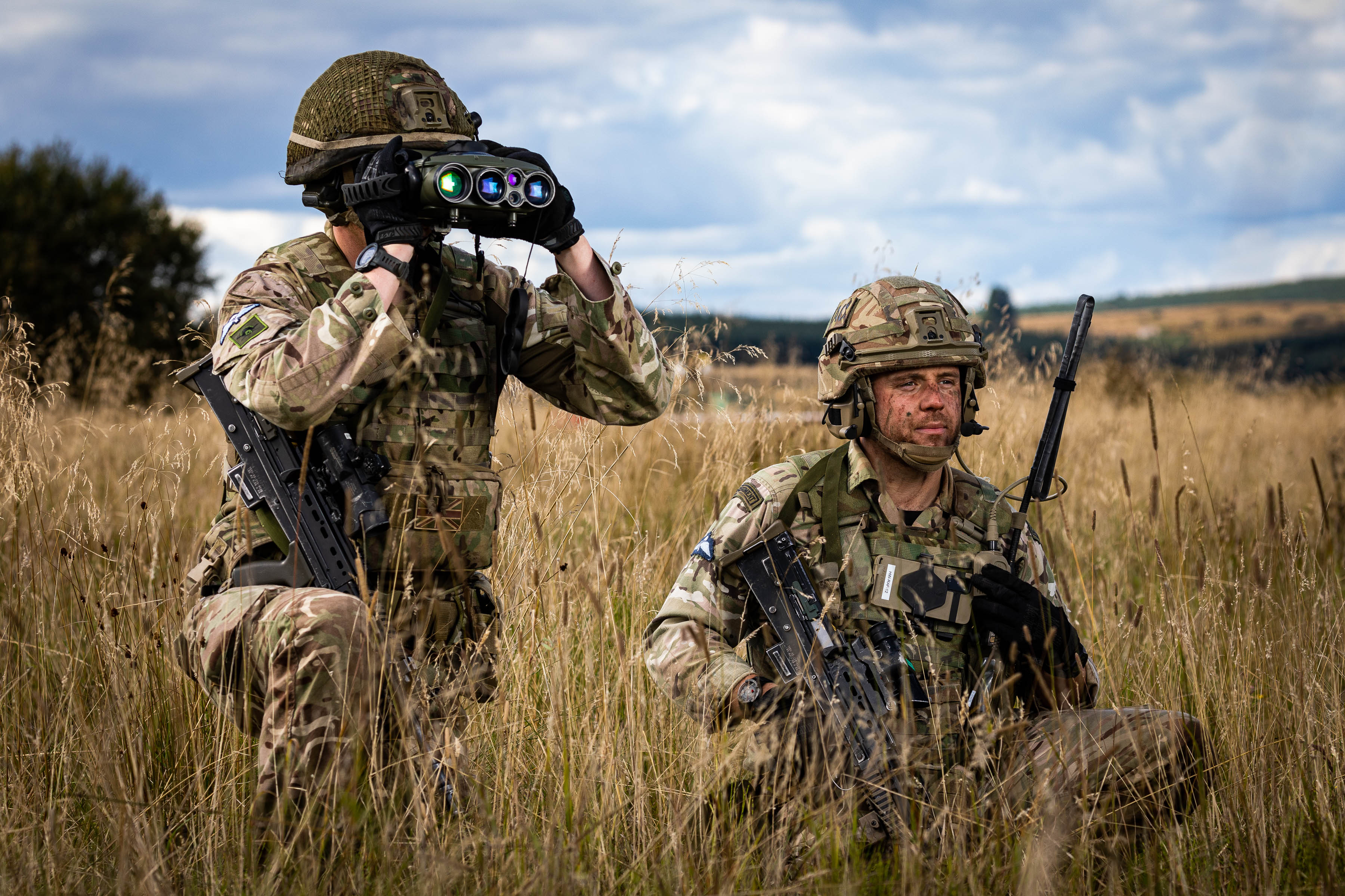 Image shows RAF personnel kneeling in field with binoculars.