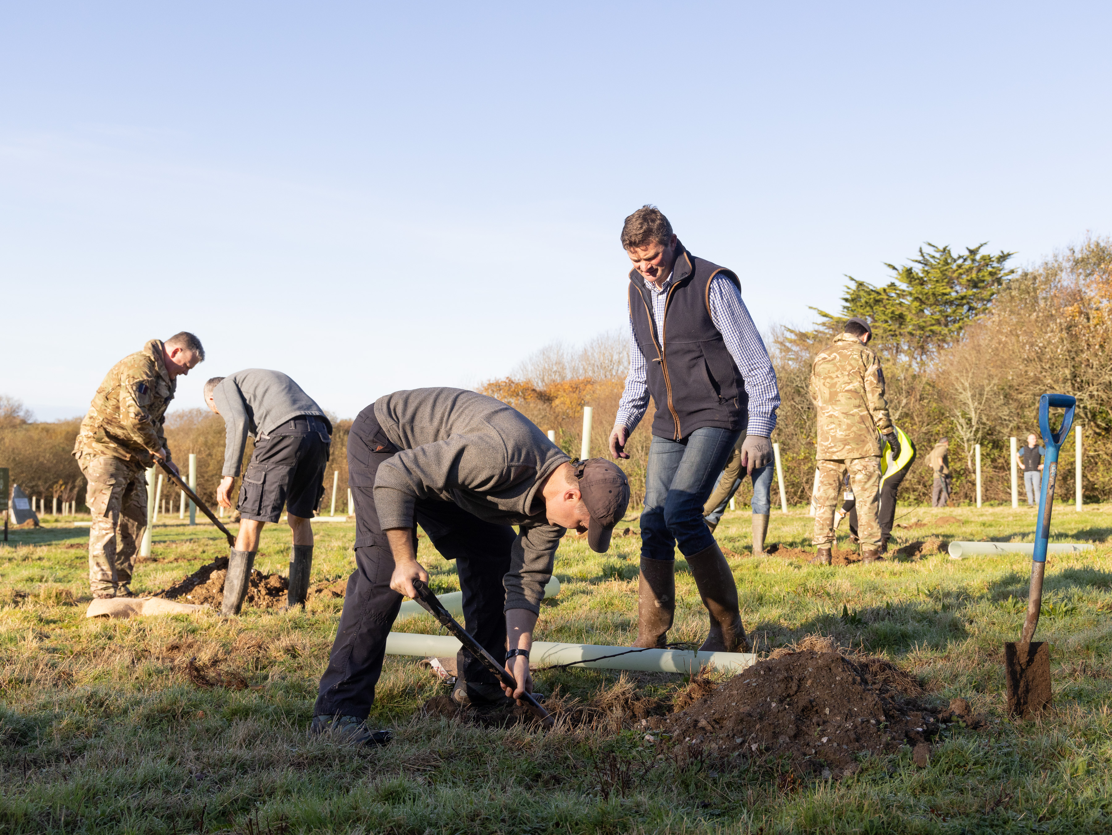 Image shows community and RAF aviators planting young trees and digging with spades.