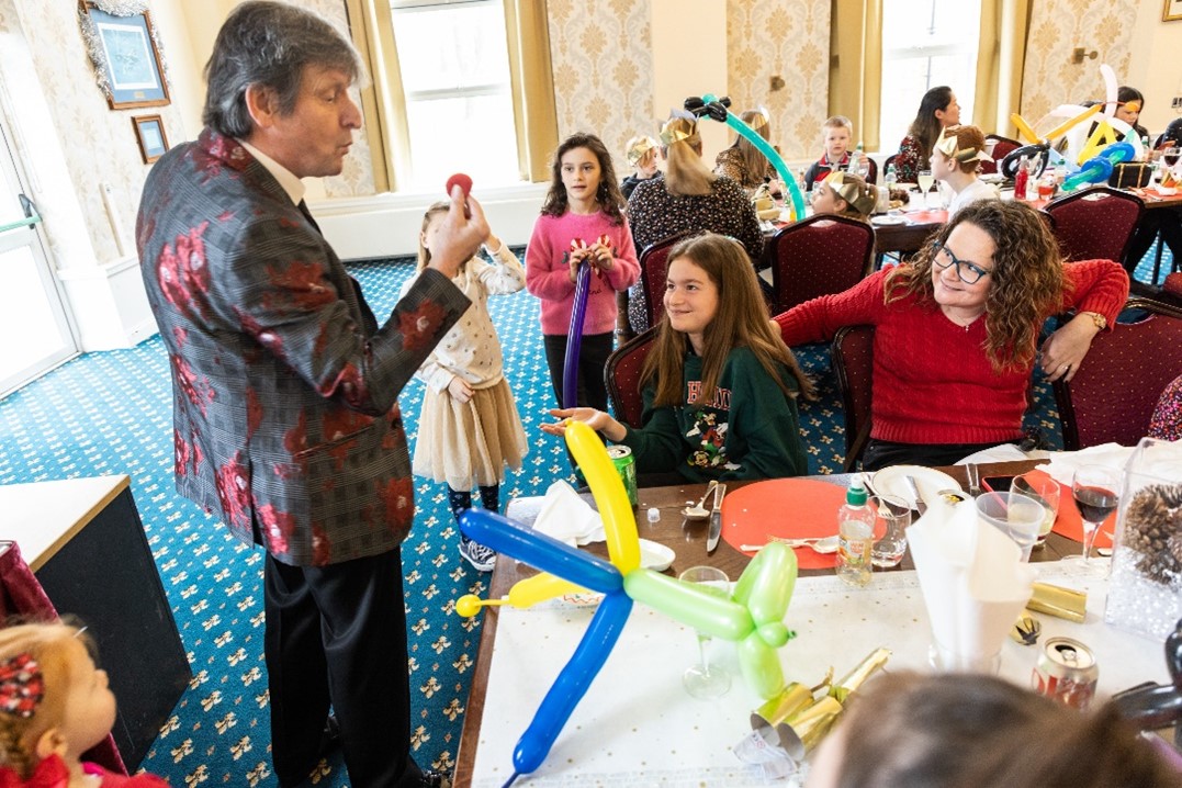 Image shows magician entertaining families with balloons at a Christmas Dinner