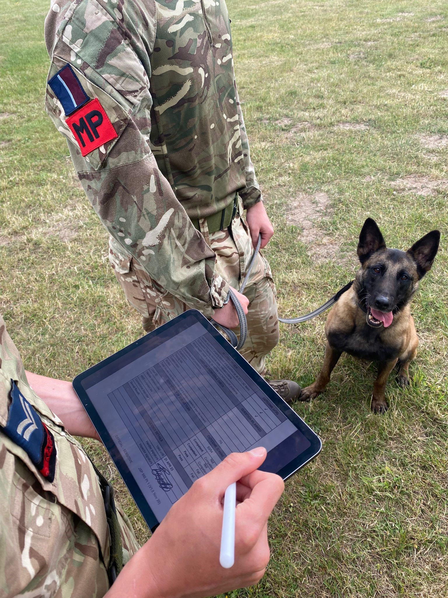 Image shows RAF Police Officer holding a digital tablet with another officer and dog.