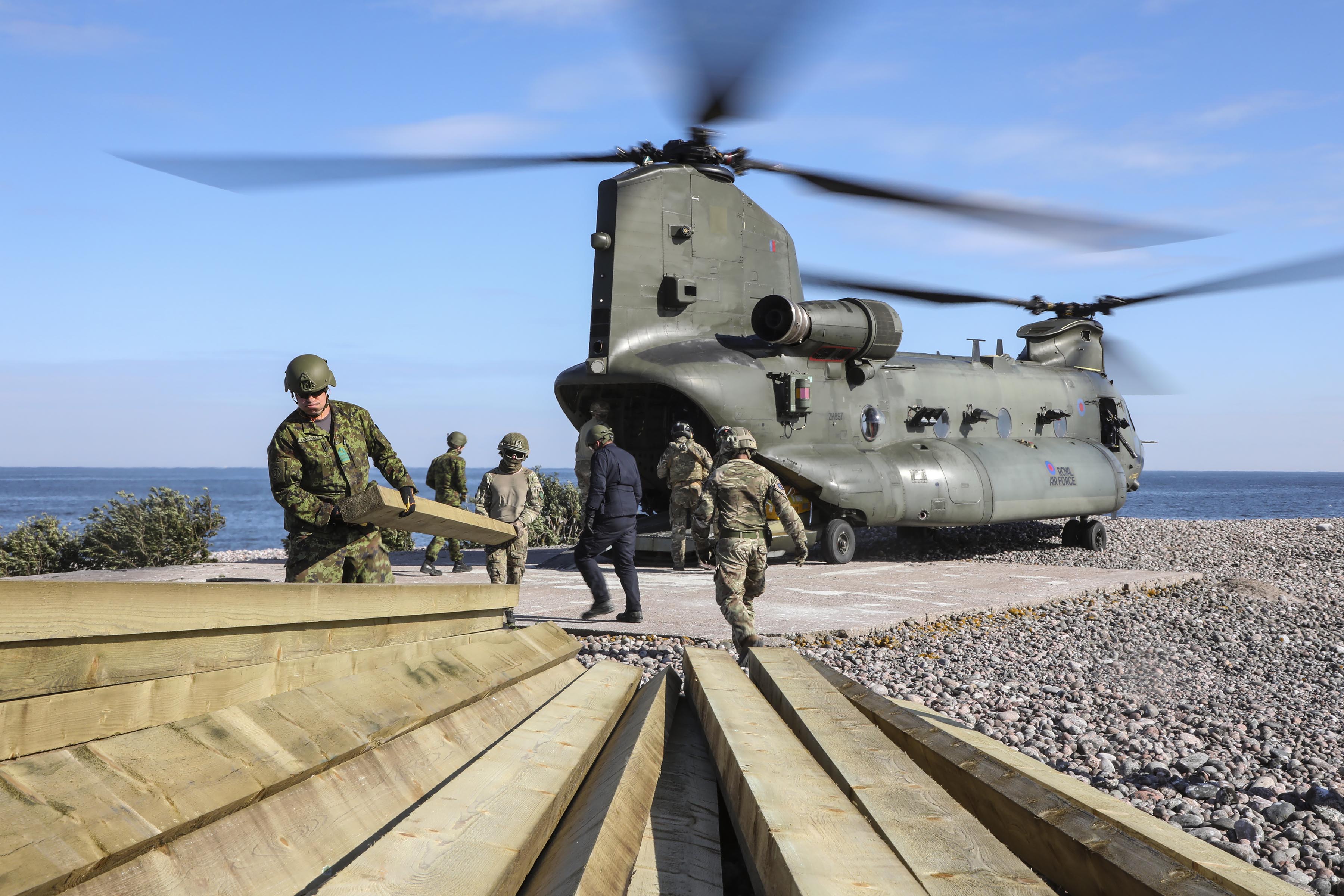 Image shows RAF Regiment carrying planks of wood on the beach, with Chinook in the background.