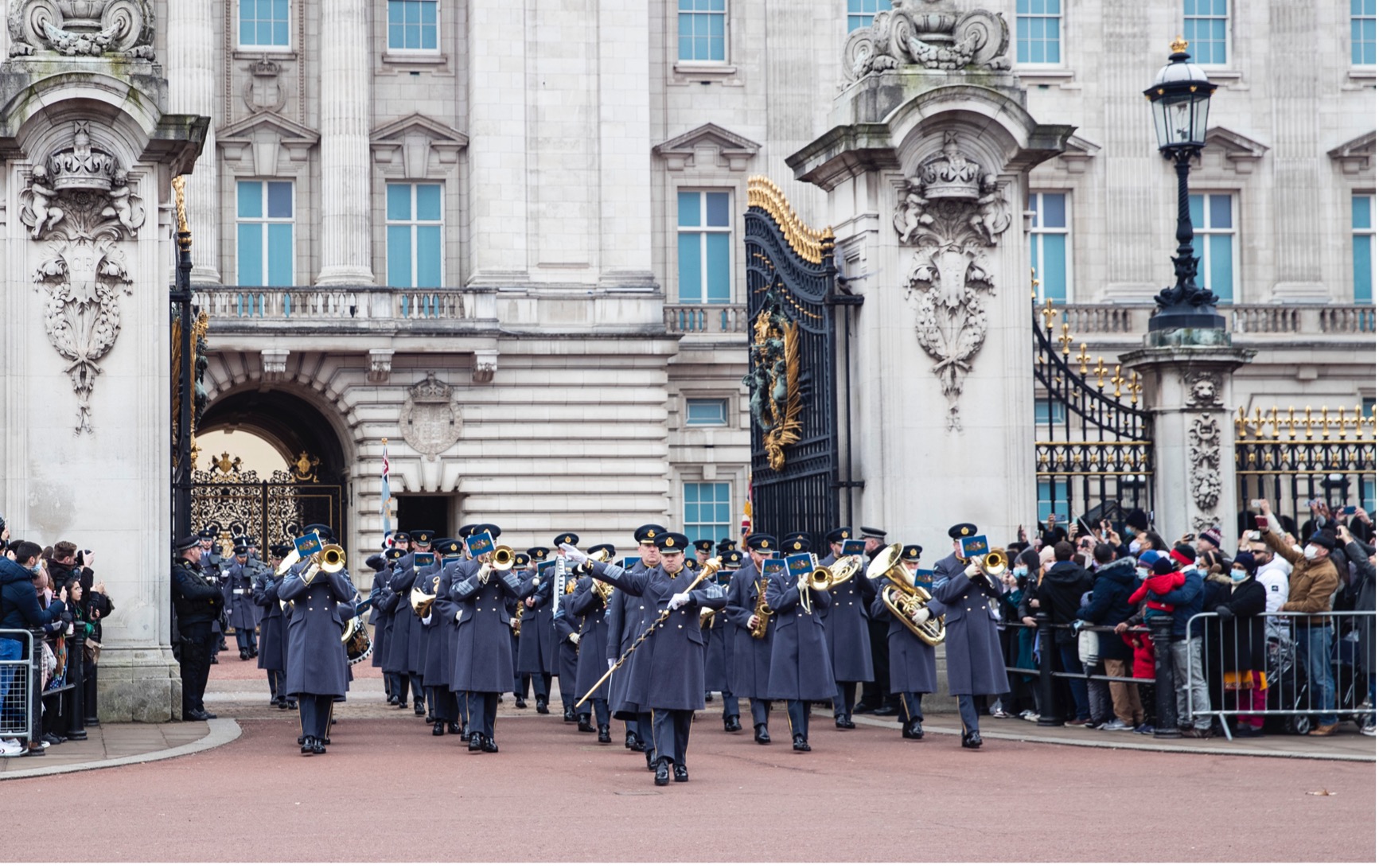 The Band of the RAF Regiment parading through gates of Buckingham Palace with public in the crowd