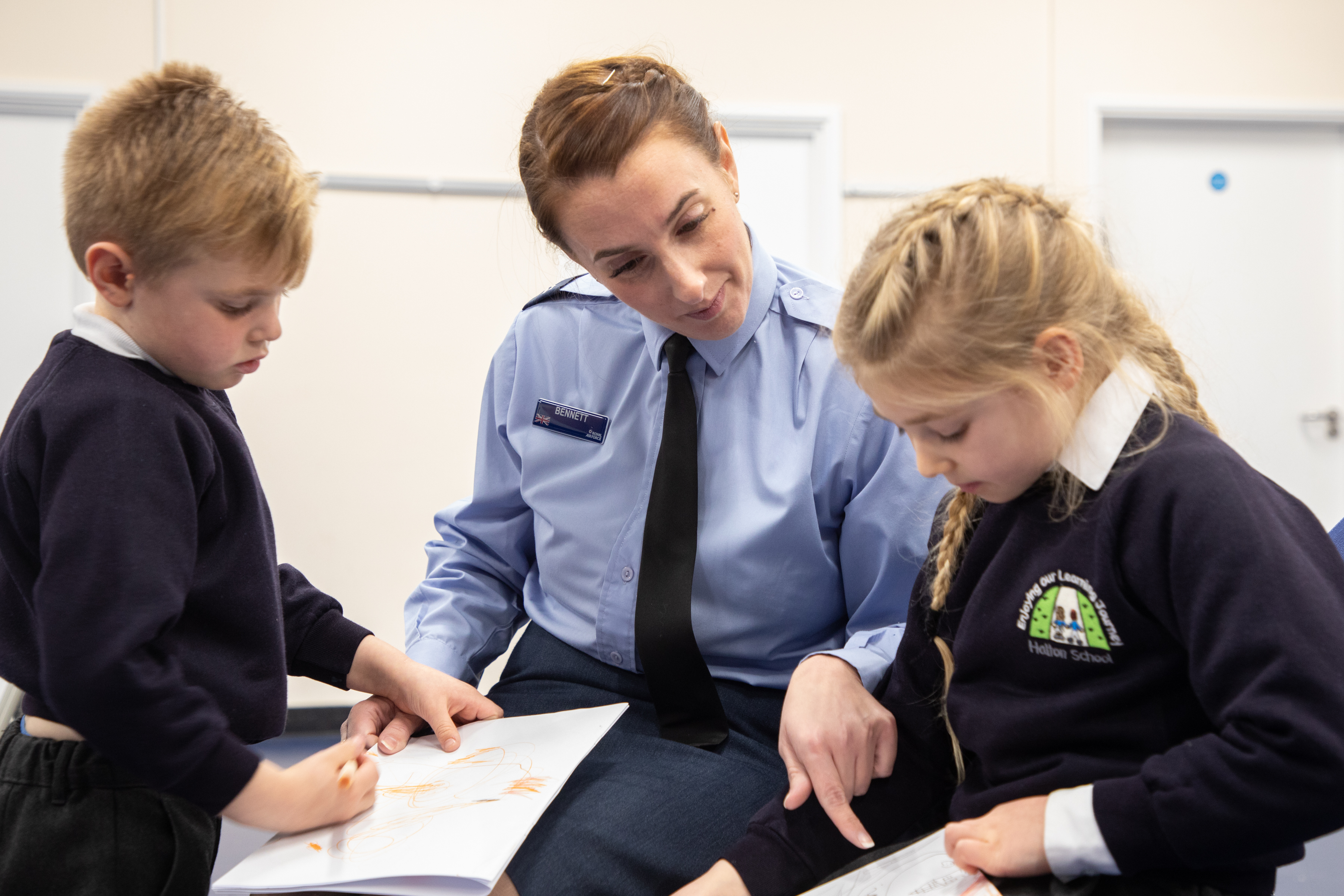 Image shows RAF aviator with school children writing.