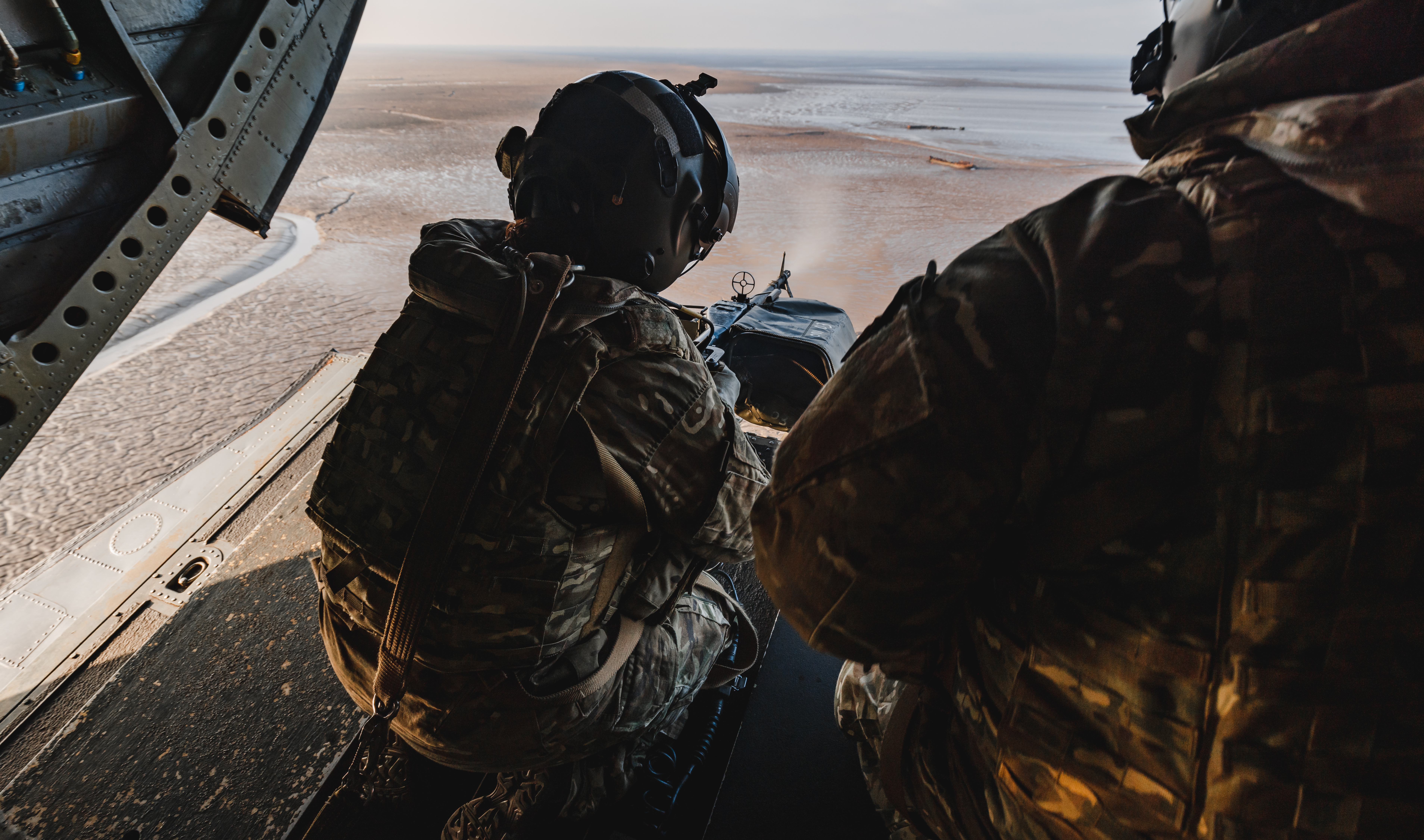 Image shows RAF Gunner manning machine gun from the back of a Chinook while it is in flight.