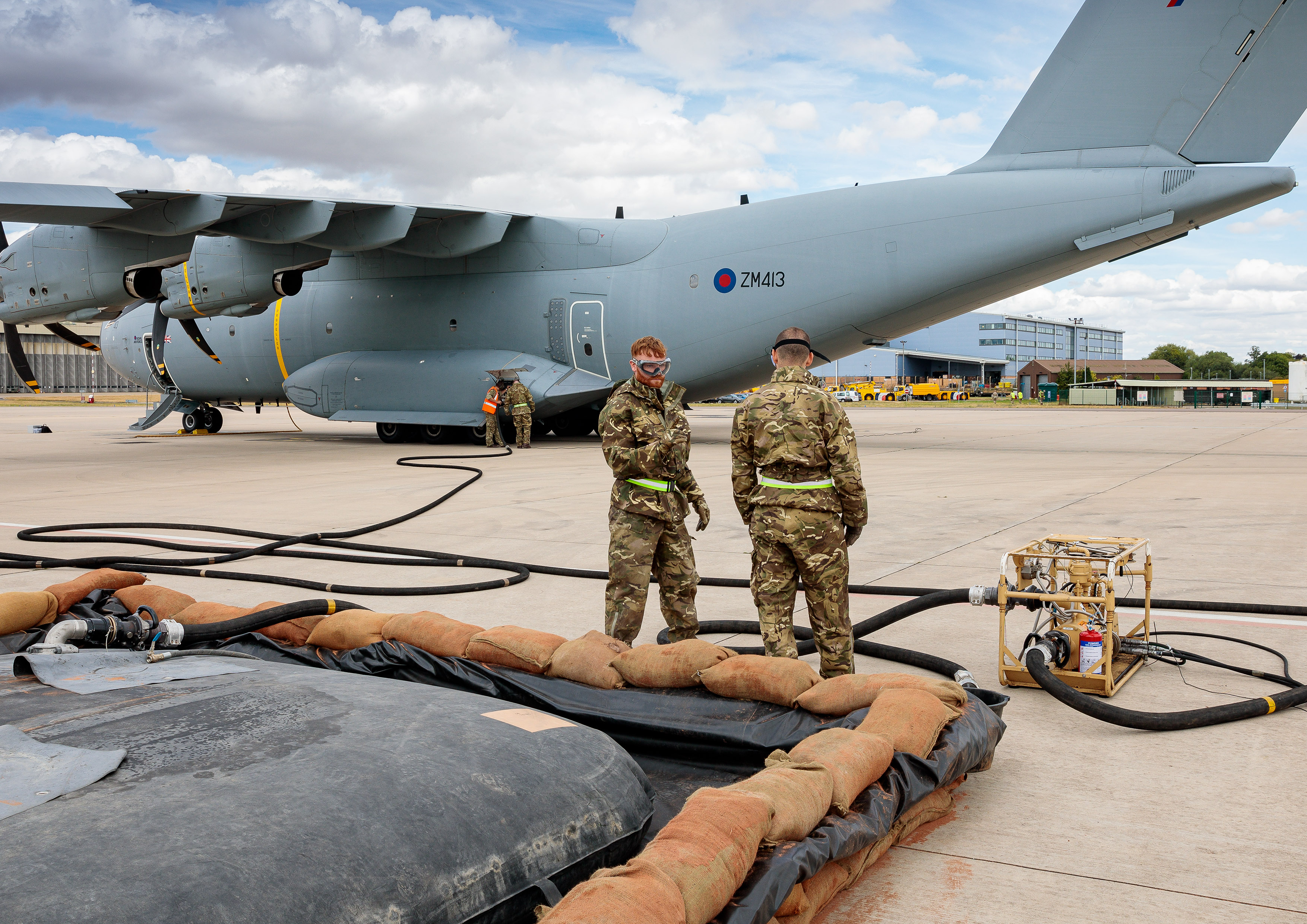 Image shows RAF aviators standing by spill kit barrier with Hercules aircraft in background. 