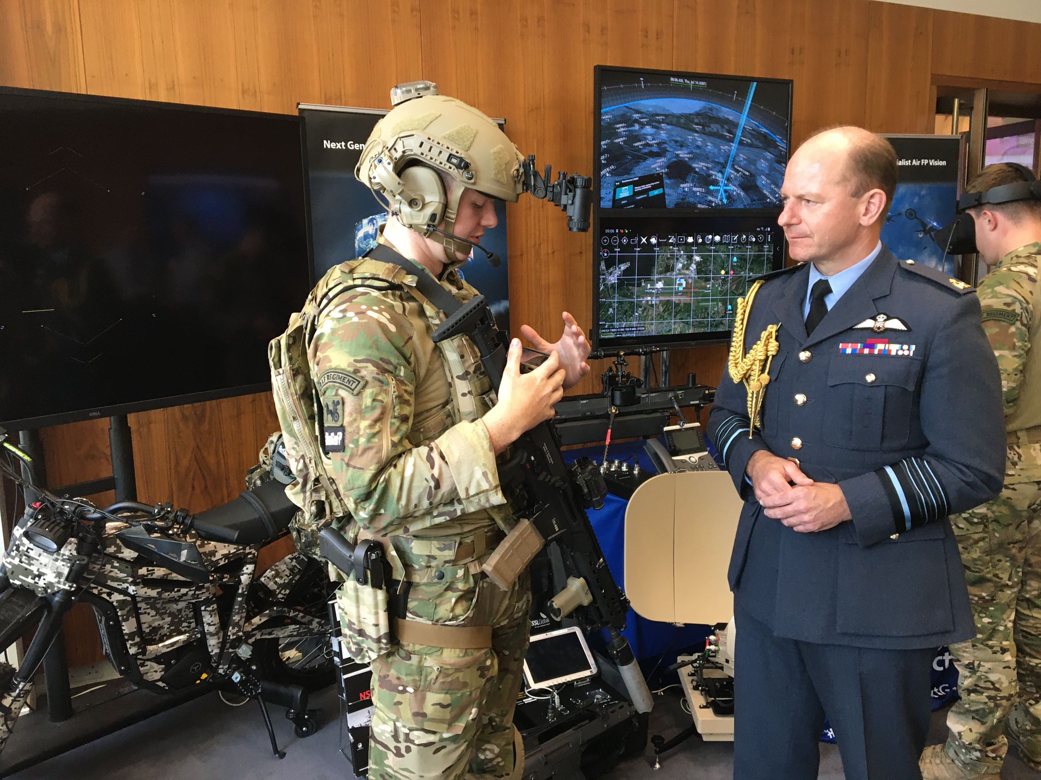 Image shows the Chief of the Air Staff talking with aviators. Room also has motorbike, technology gadgets, and computer screen too.