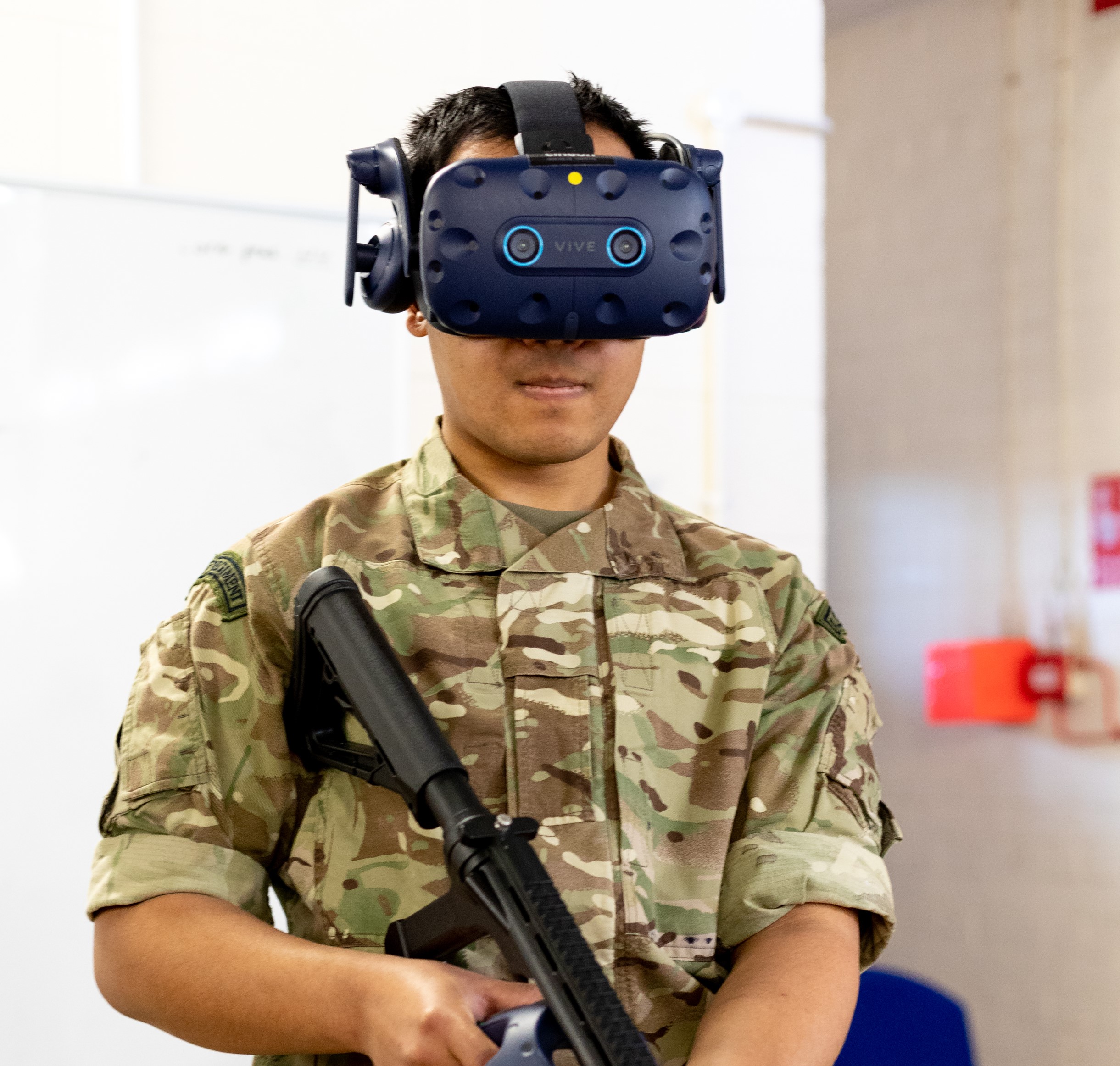 Image shows RAF aviator using virtual reality headset and holding rifle.