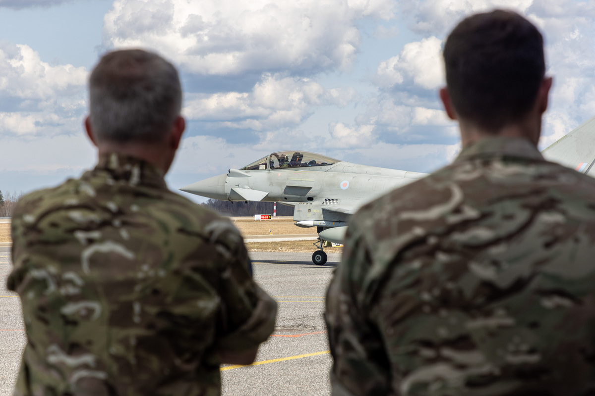 Image shows the back of two RAF personnel looking towards a RAF Typhoon.