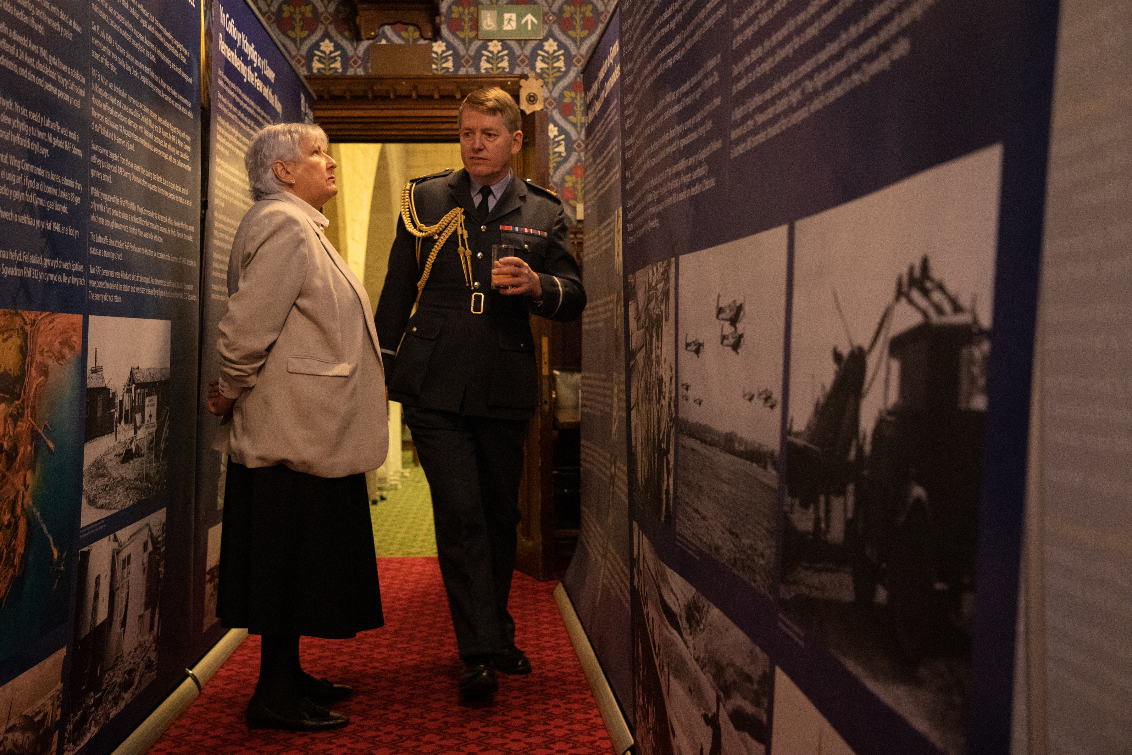 Image shows RAF aviator and civilian looking at pictures in exhibition. 