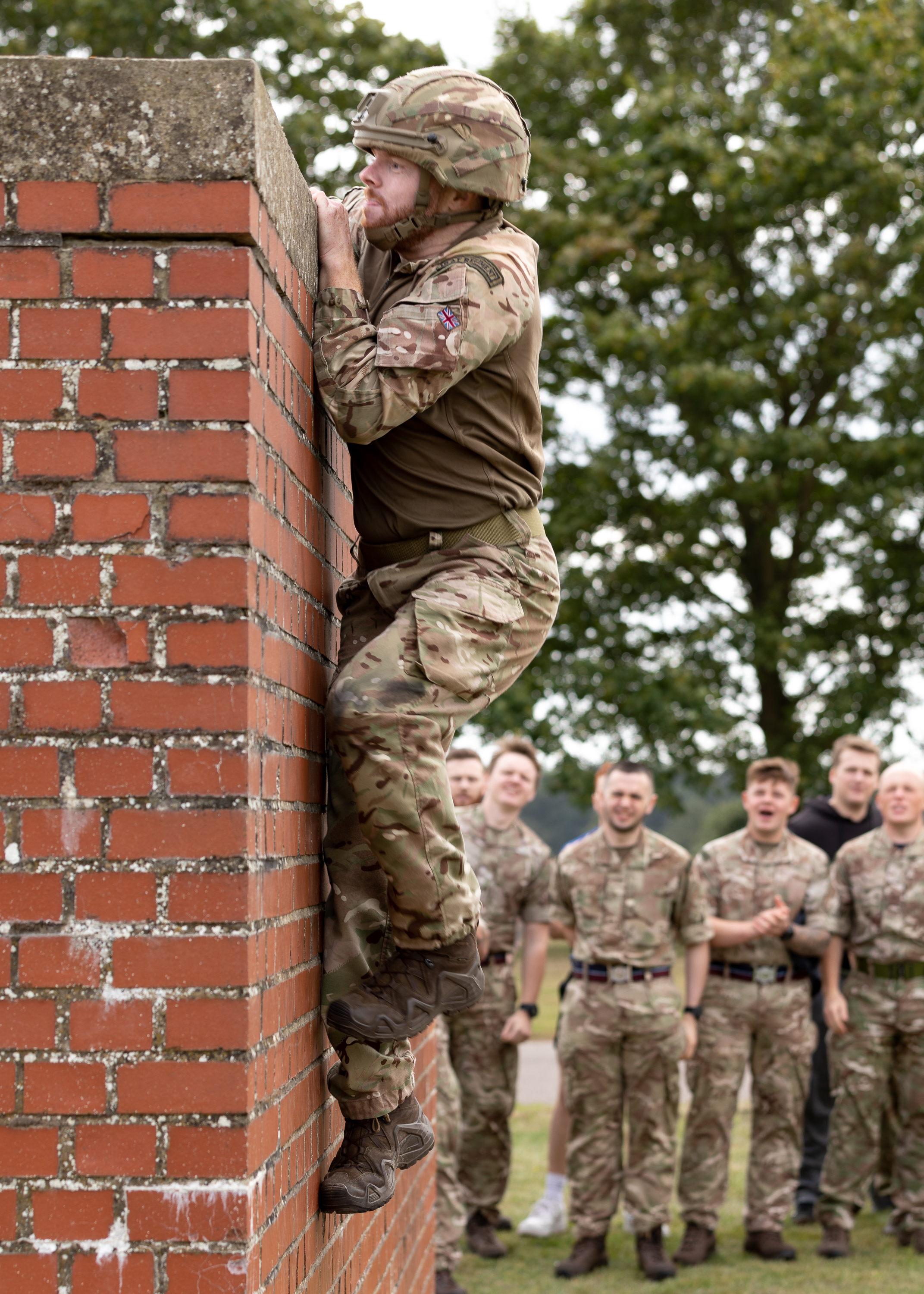 Personnel climbing a brick wall while Squadron cheers on.
