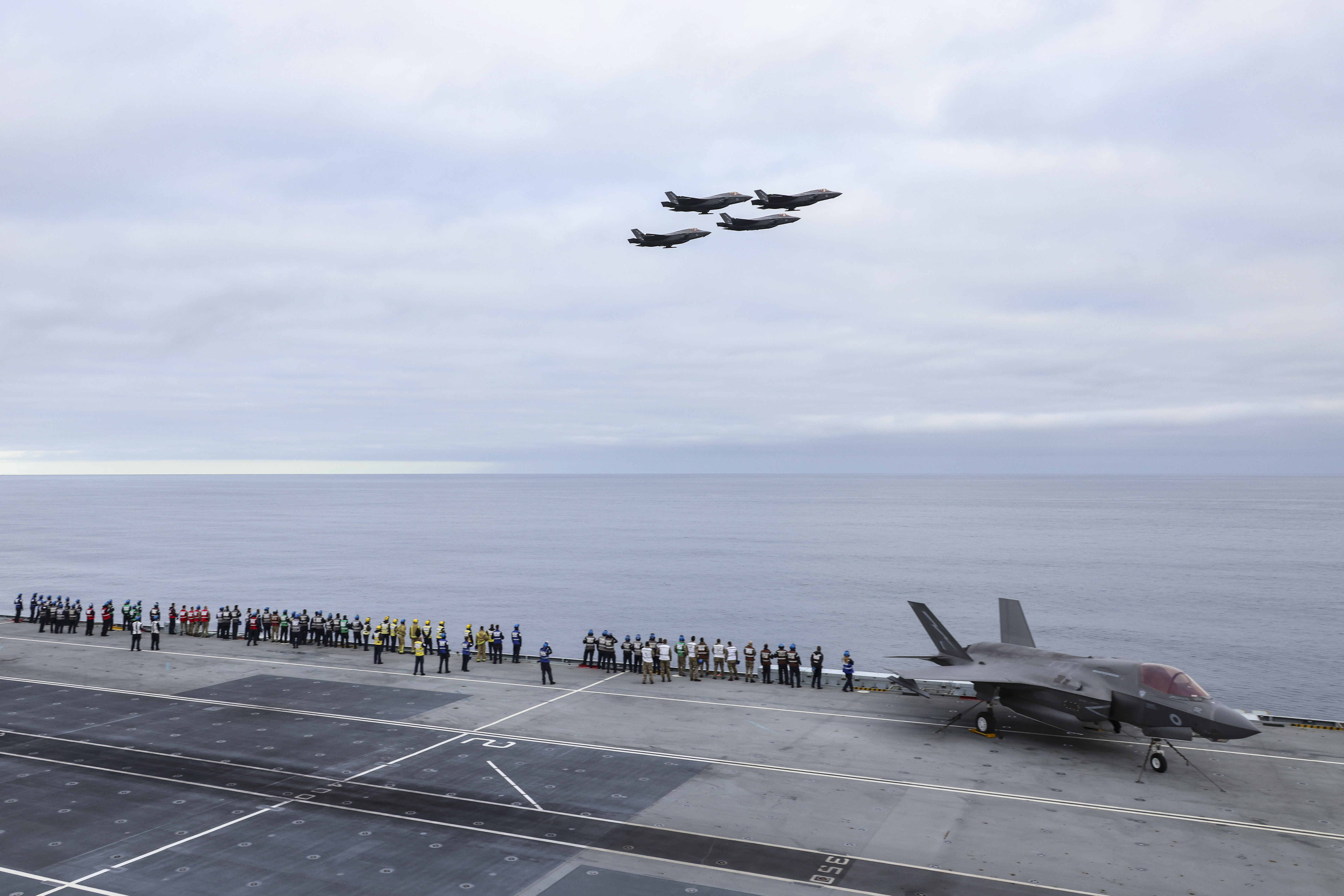 Image shows personnel and RAF Typhoons on the deck of aircraft carrier, with flypast.