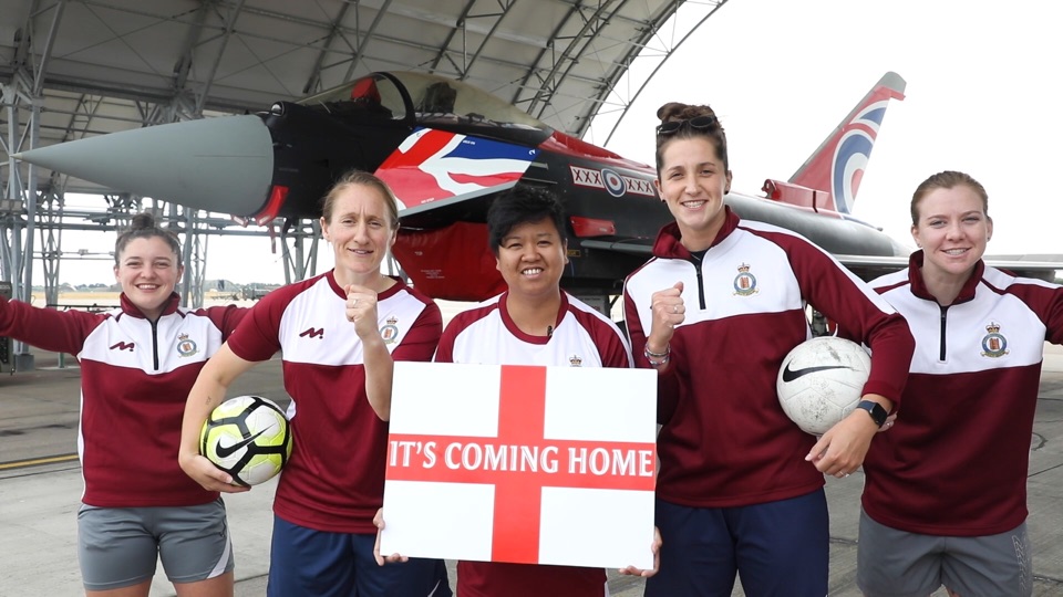 Image shows women with England an 'It's Coming Home' sign and Union Jack painted RAF Typhoon.