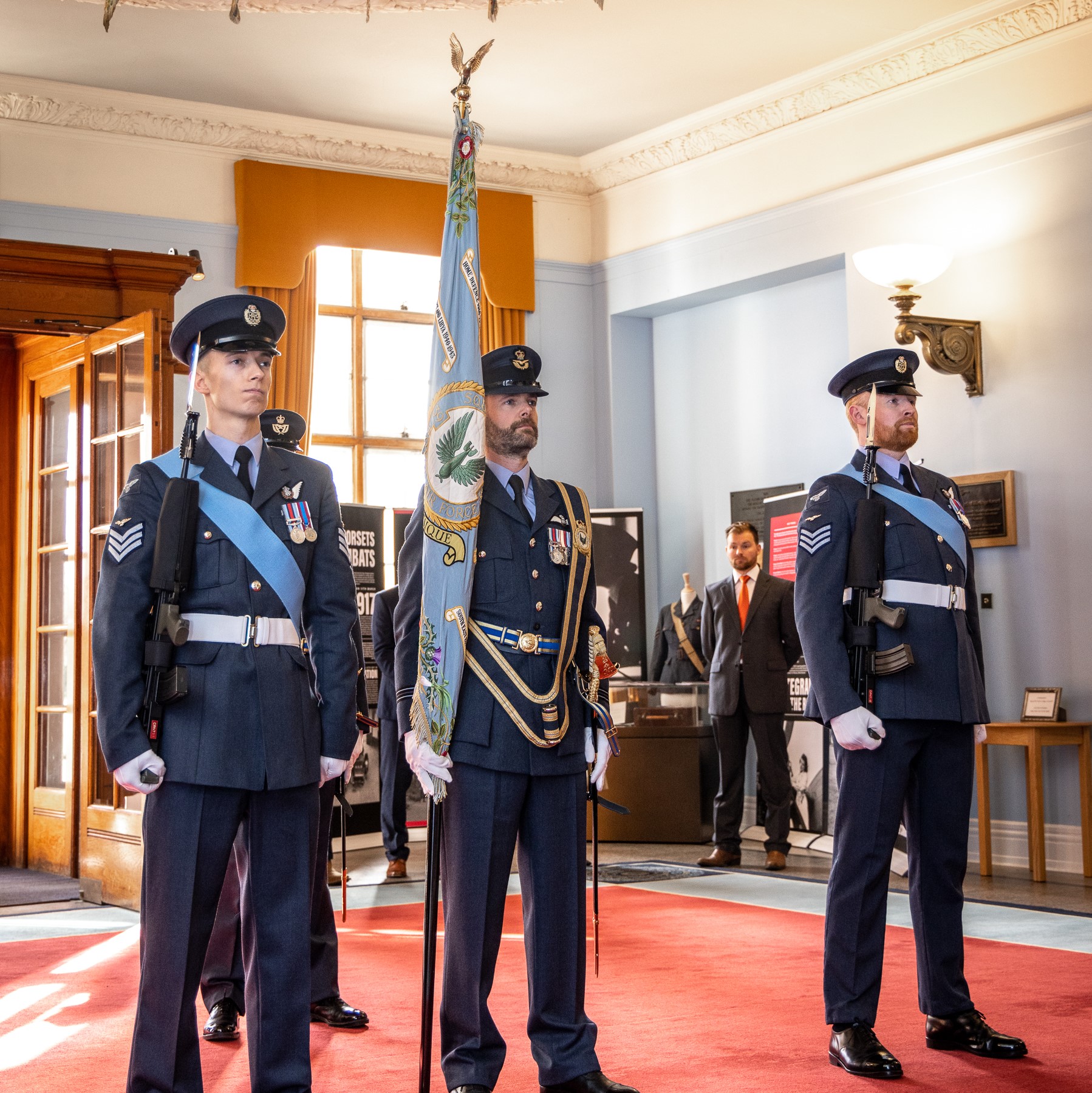 Image shows RAF aviators with colour standard inside Officers' Mess during ceremony.
