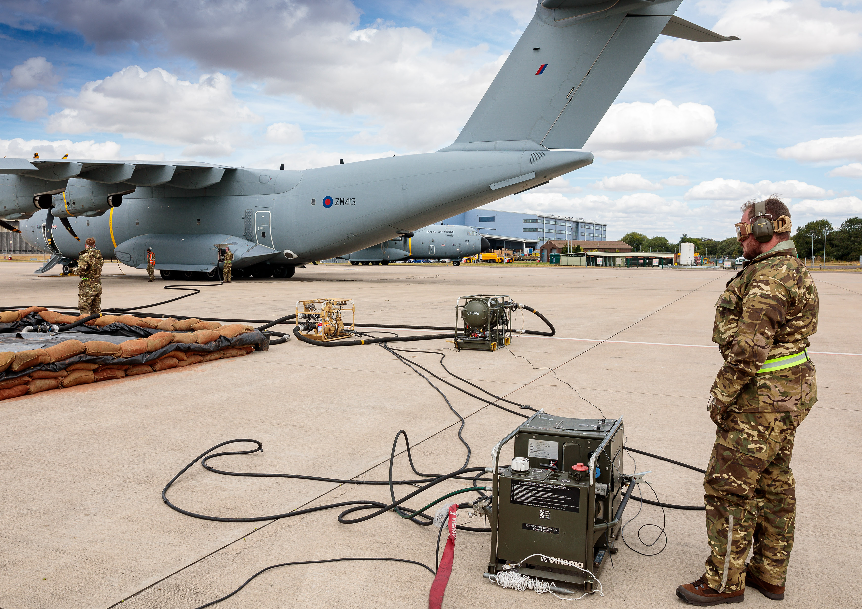 Image shows RAF aviators standing by spill kit barrier and refuelling equipment with Hercules aircraft in background. 