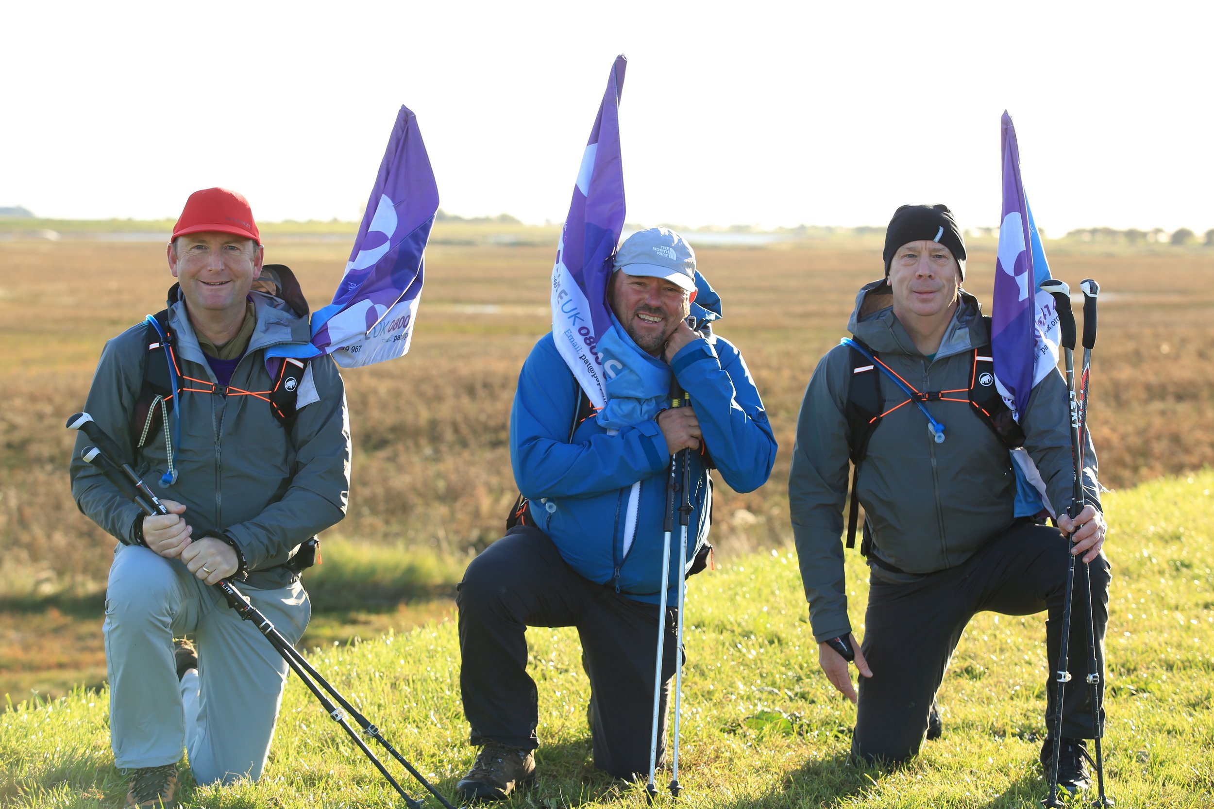 Image shows three dads kneeling with hiking poles and flags.