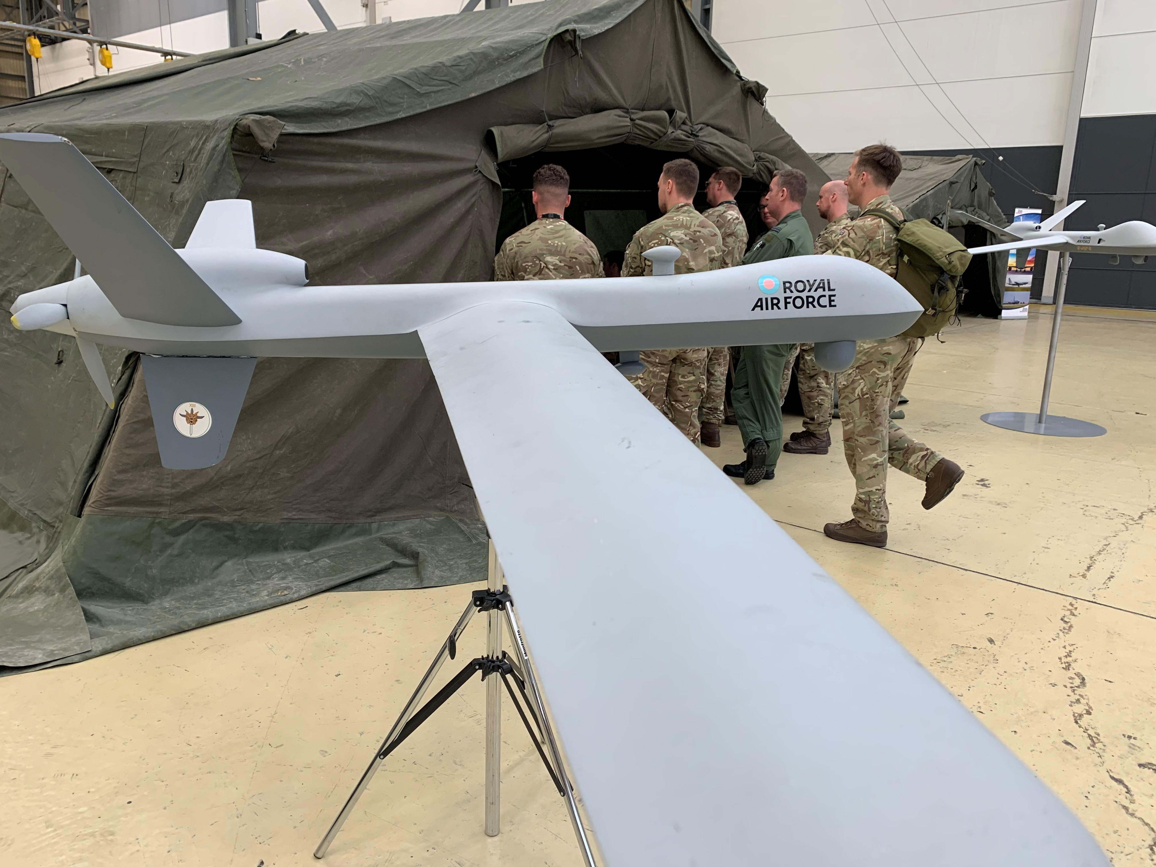 Model aircraft of RAF Reaper with Aviators walking into indoor tent structure.