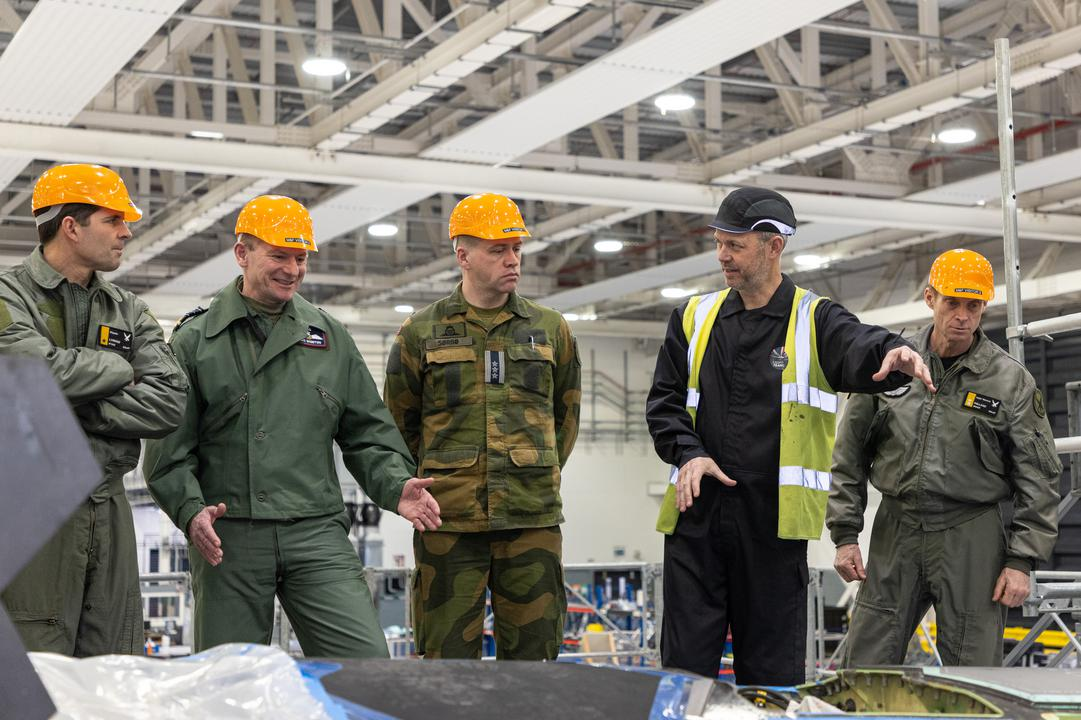 Image shows personnel discussing inside a hangar wearing hard hats;