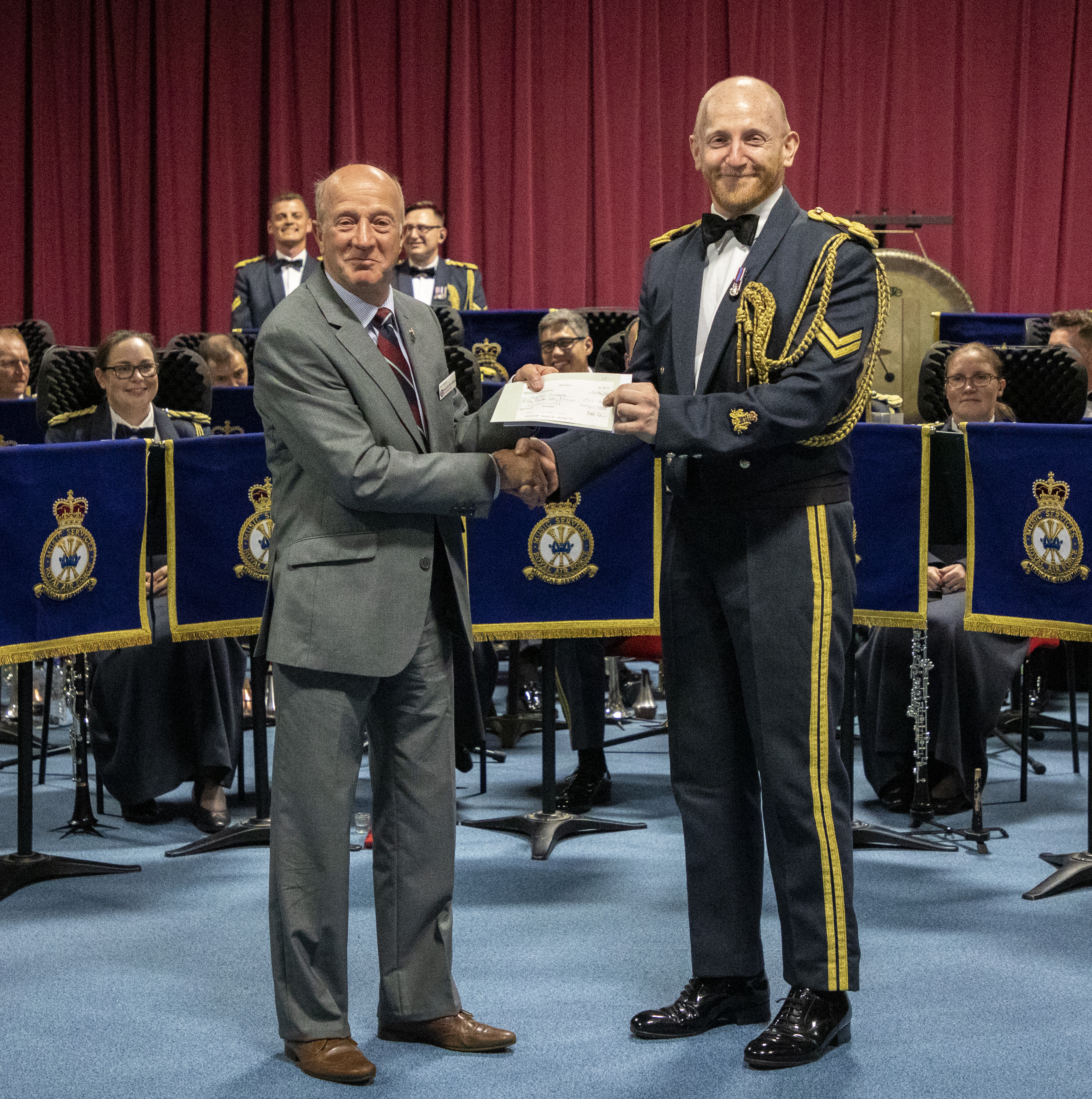 RAF Musician is presented with certificate awards by Adjudicator, and Band in the background.