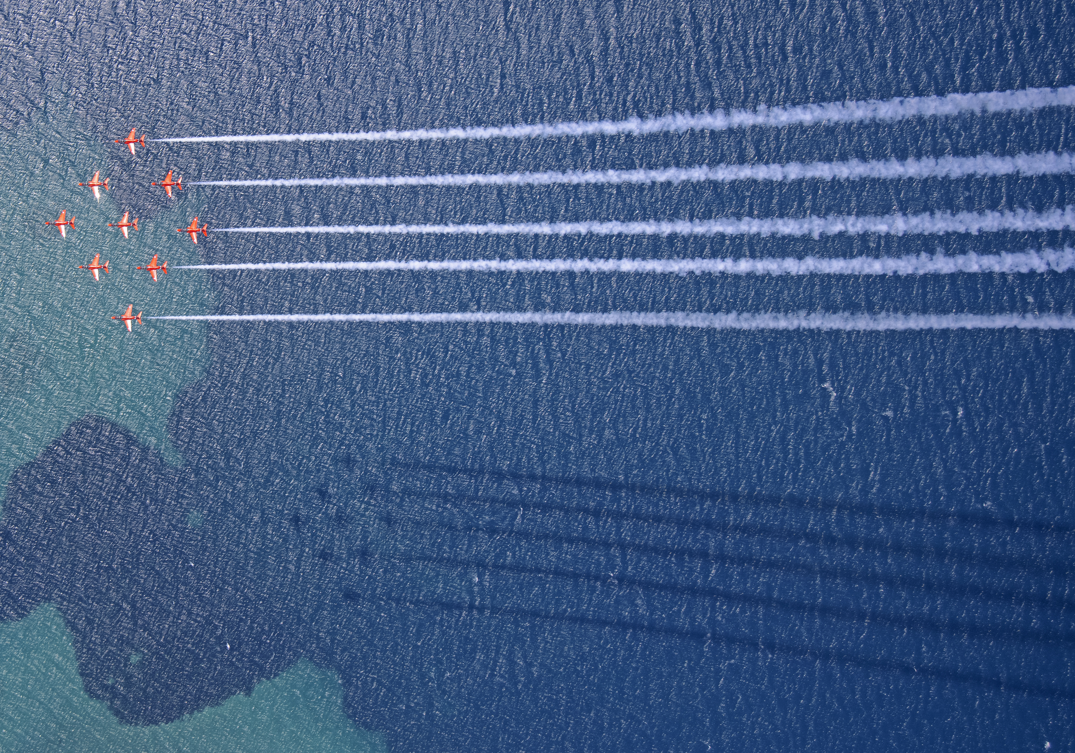 Red Arrows in formation over the water, with smoke trails.