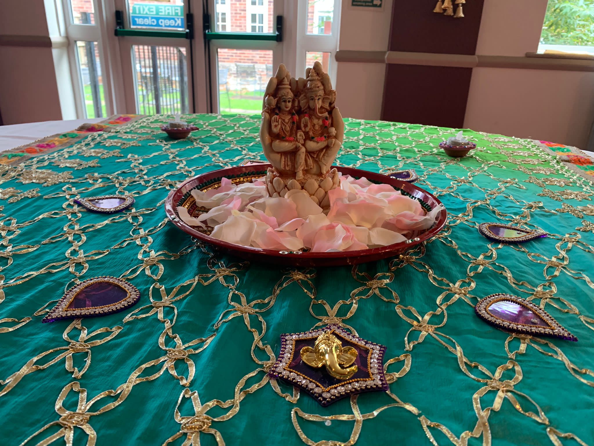 Image shows traditional Diwali decorations on a tables with a Hindi god statue and rose petals.