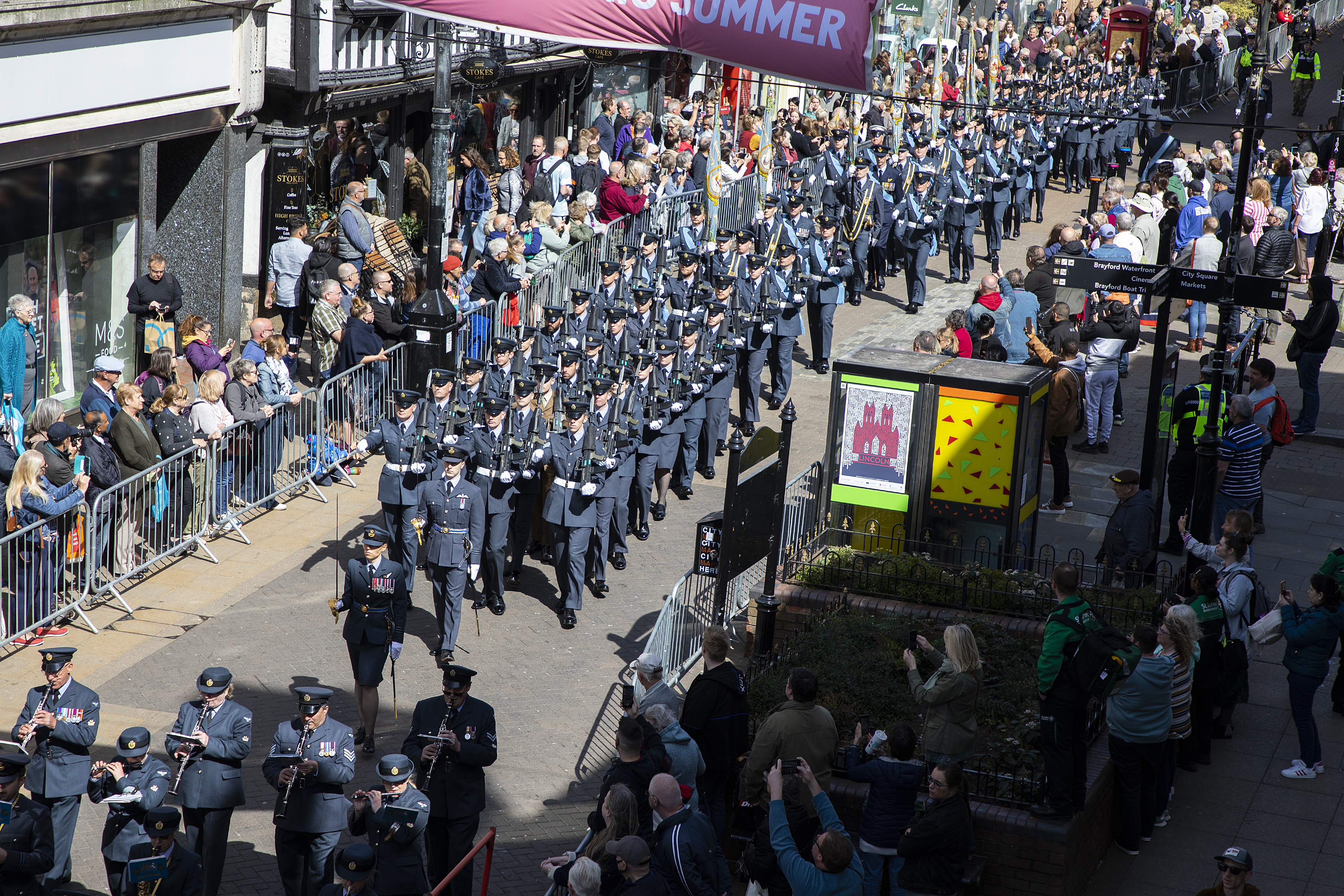 Personnel parade through the street, with public behind barriers.