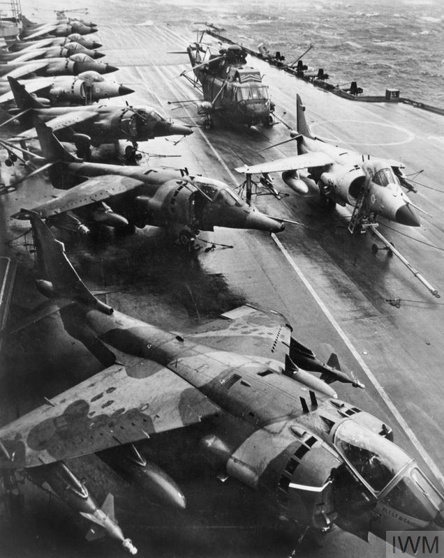 Old photo of a Harrier GR.3 aircraft and Royal Navy Sea Harriers and a Sea King helicopter on the deck of a Battleship.
