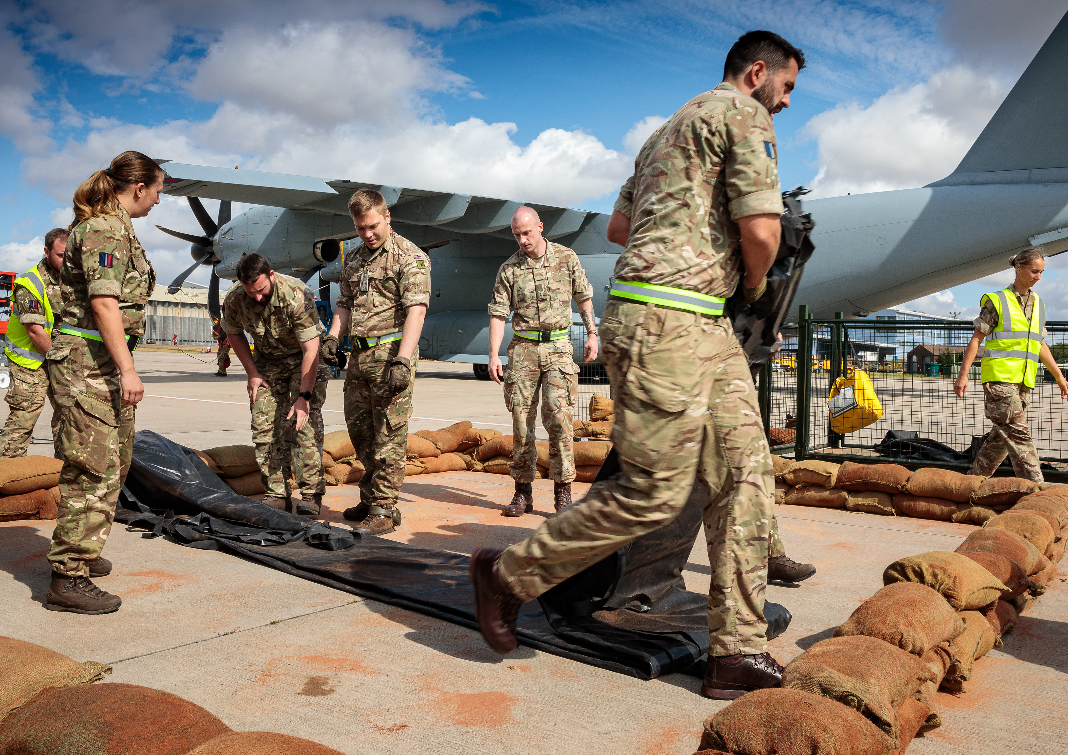 Image shows RAF aviators and sandbags barrier with Hercules aircraft in background. 