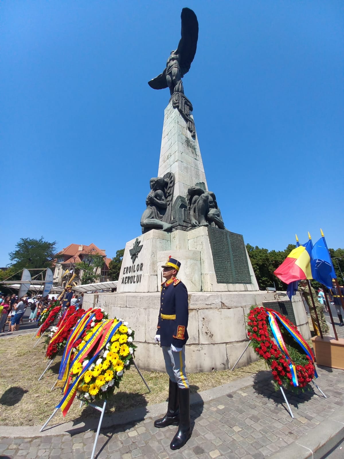 Image shows Romanian soldier standing by poppy wreaths and statue.