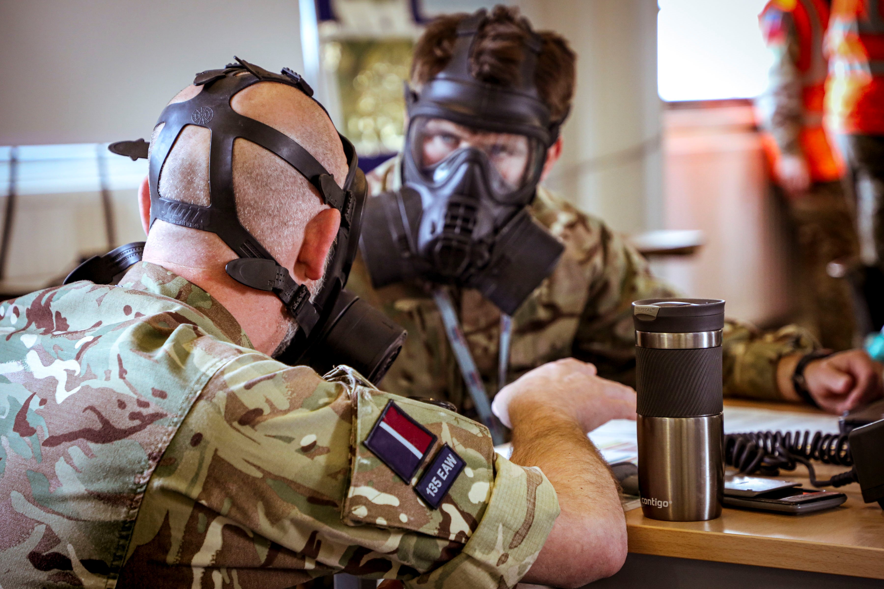 Image shows two RAF aviators wearing a respiratory gas mask at a table..