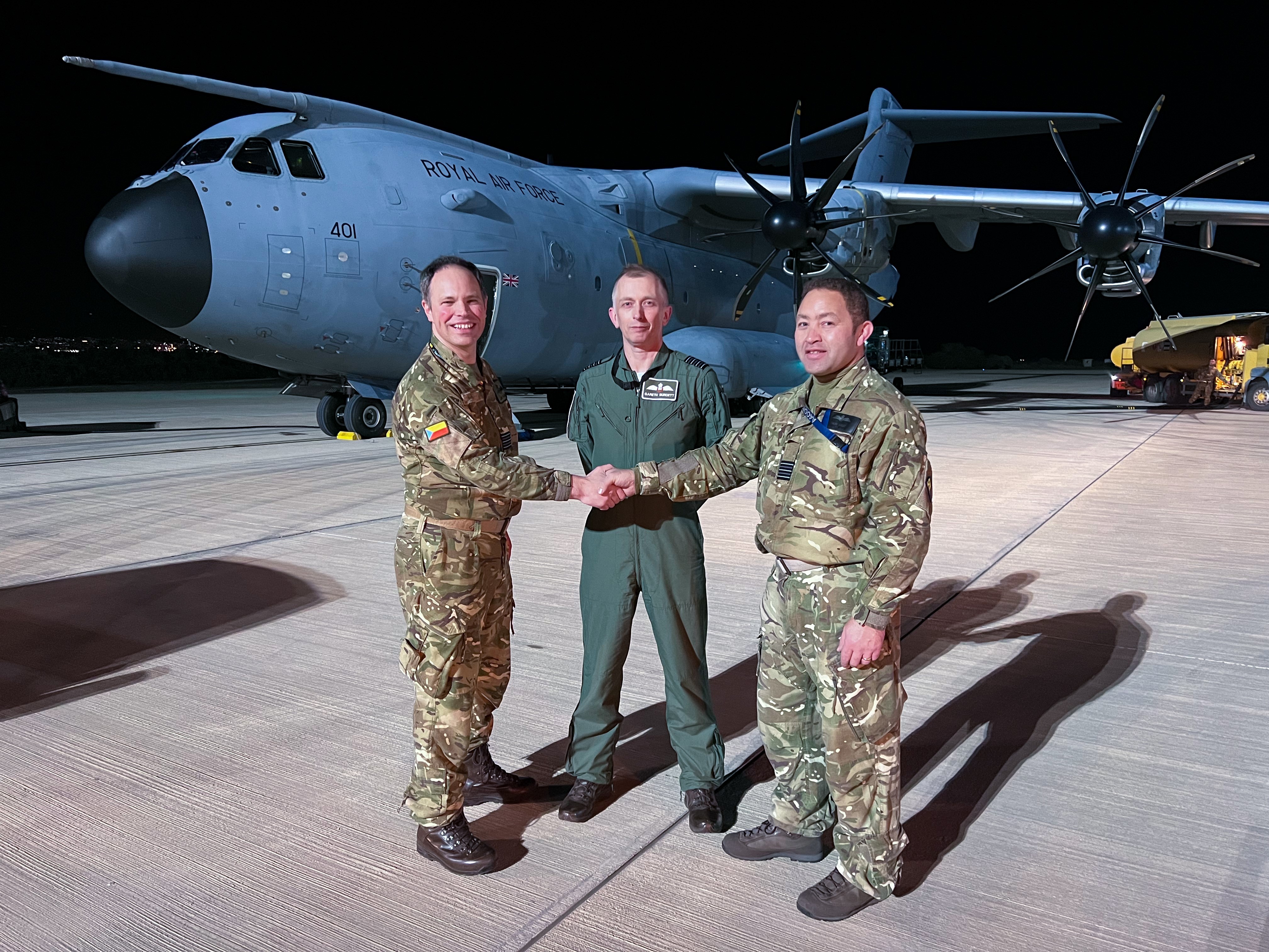 Image shows three RAF aviators shaking hands in by a RAF Hercules aircraft, on the airfield at night.
