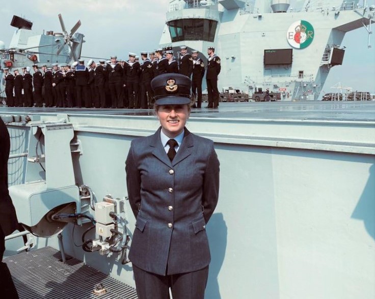 Image shows RAF aviator with HMS Battleship and Royal Navy Squadron behind her.