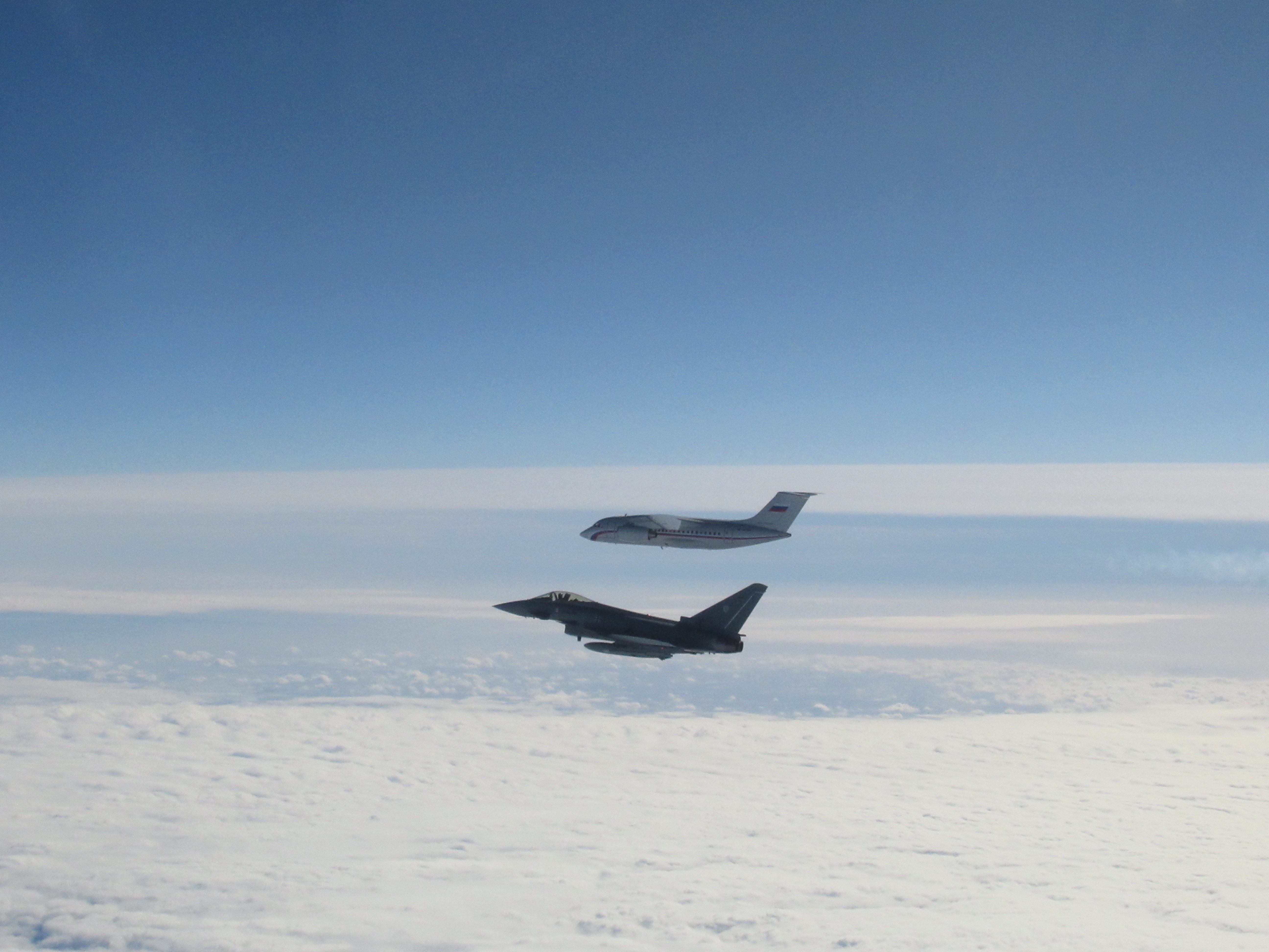 Image shows RAF Typhoon and Russian aircraft in flight above clouds.