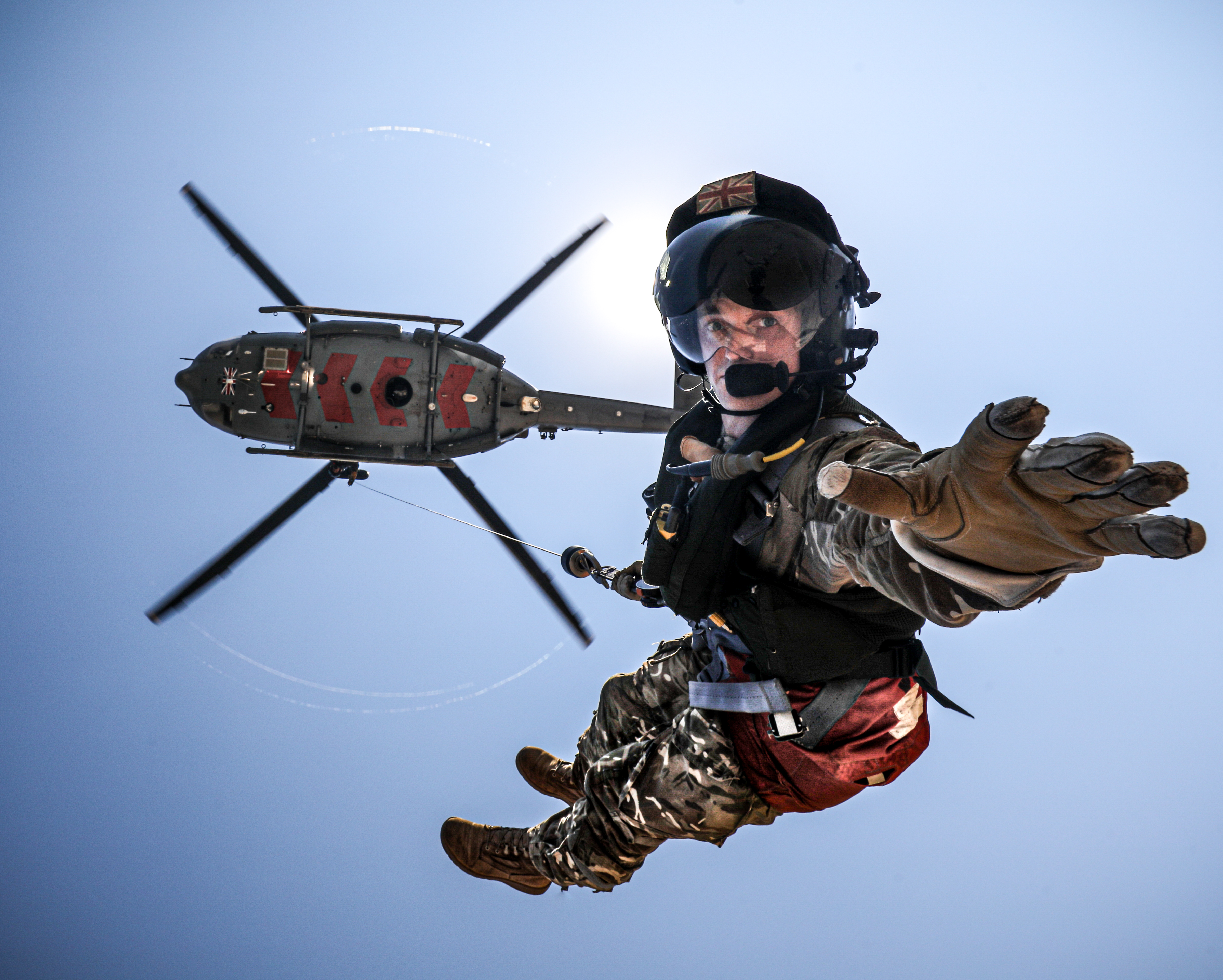 Image shows RAF aviator reaching towards camera as he repels down from helicopter.