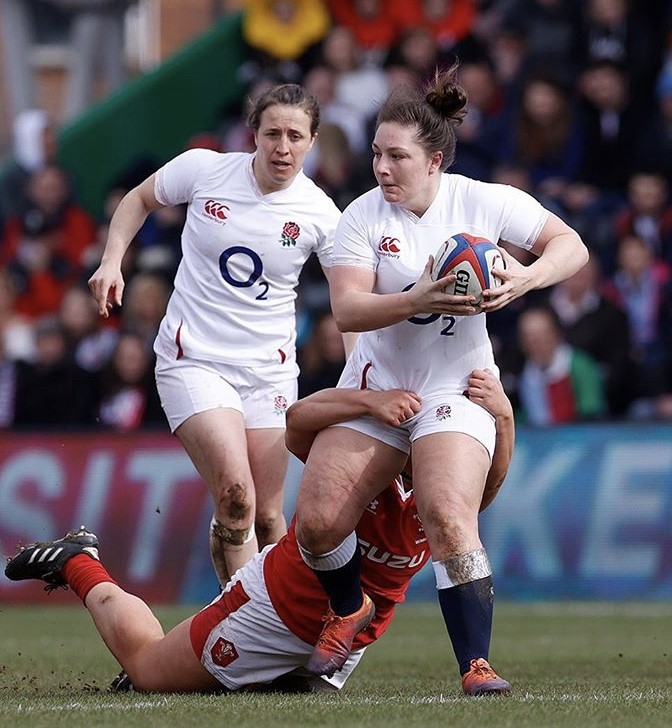 Image shows two female rugby players and another mid tackle.