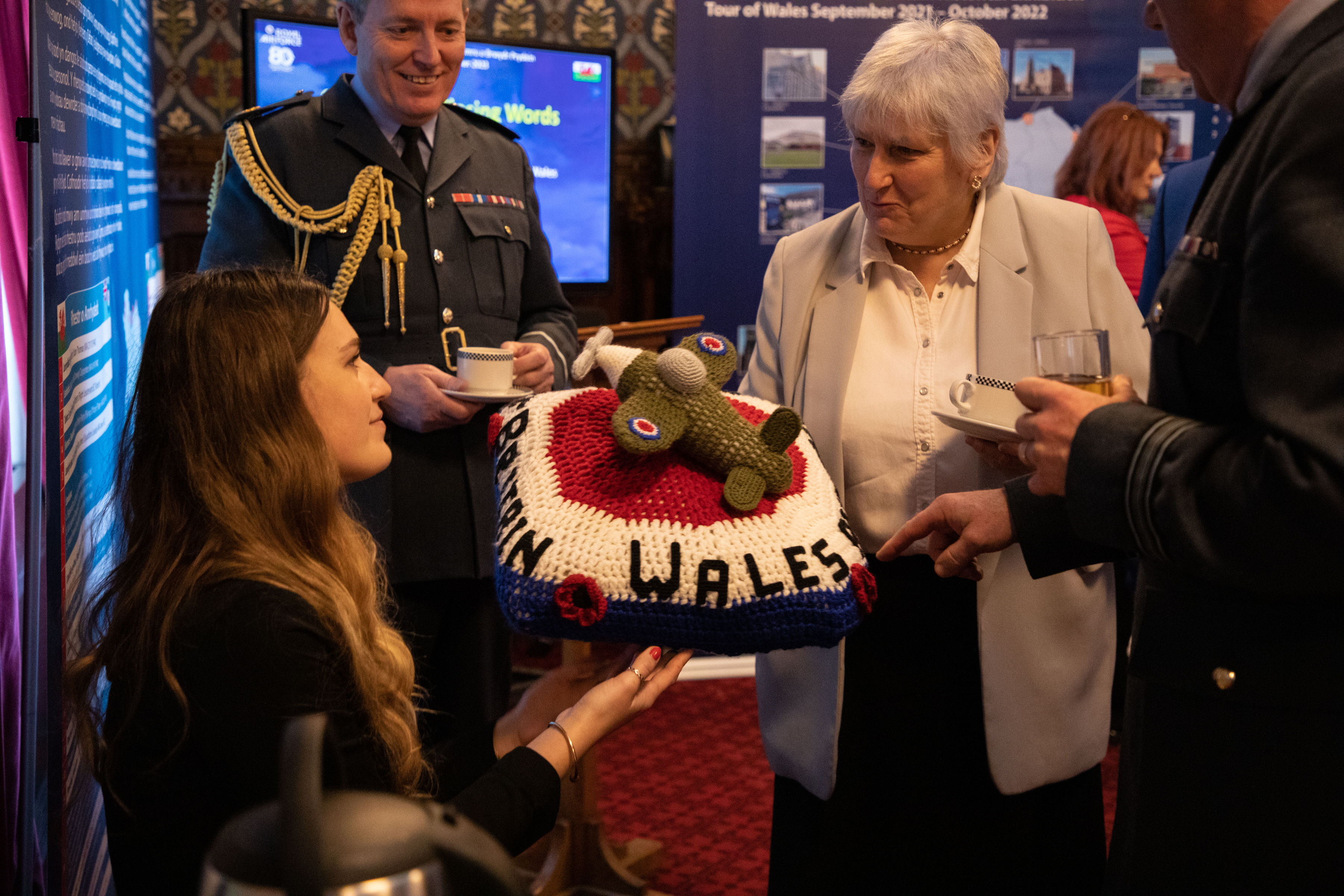 Image shows RAF aviator and civilians holding a crocheted Spitfire model at the exhibition.