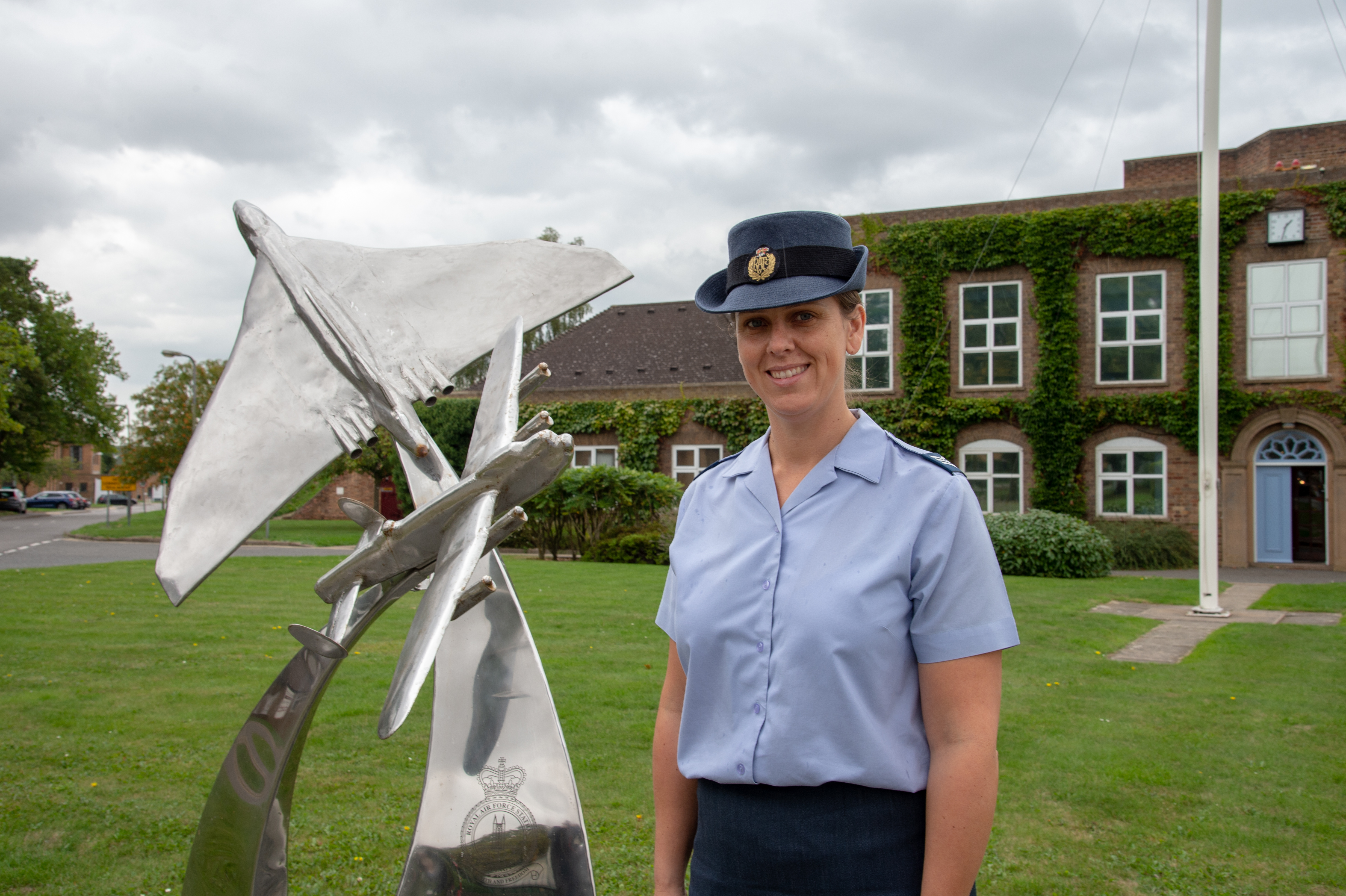 Image shows RAF aviator standing by a metal aircraft statue outside.. 