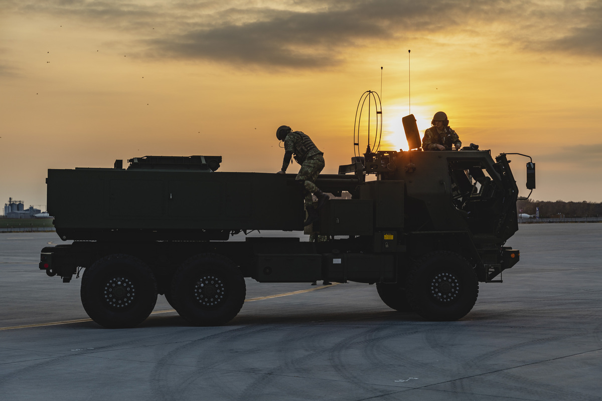 Image shows truck with personnel climbing out, on an airfield.during sunset.