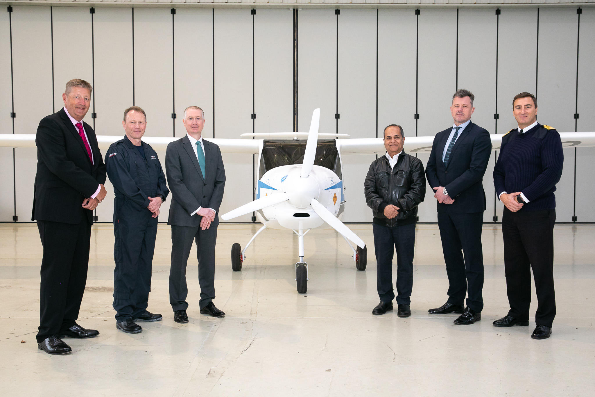 Pilots stand with electric aircraft inside hangar.