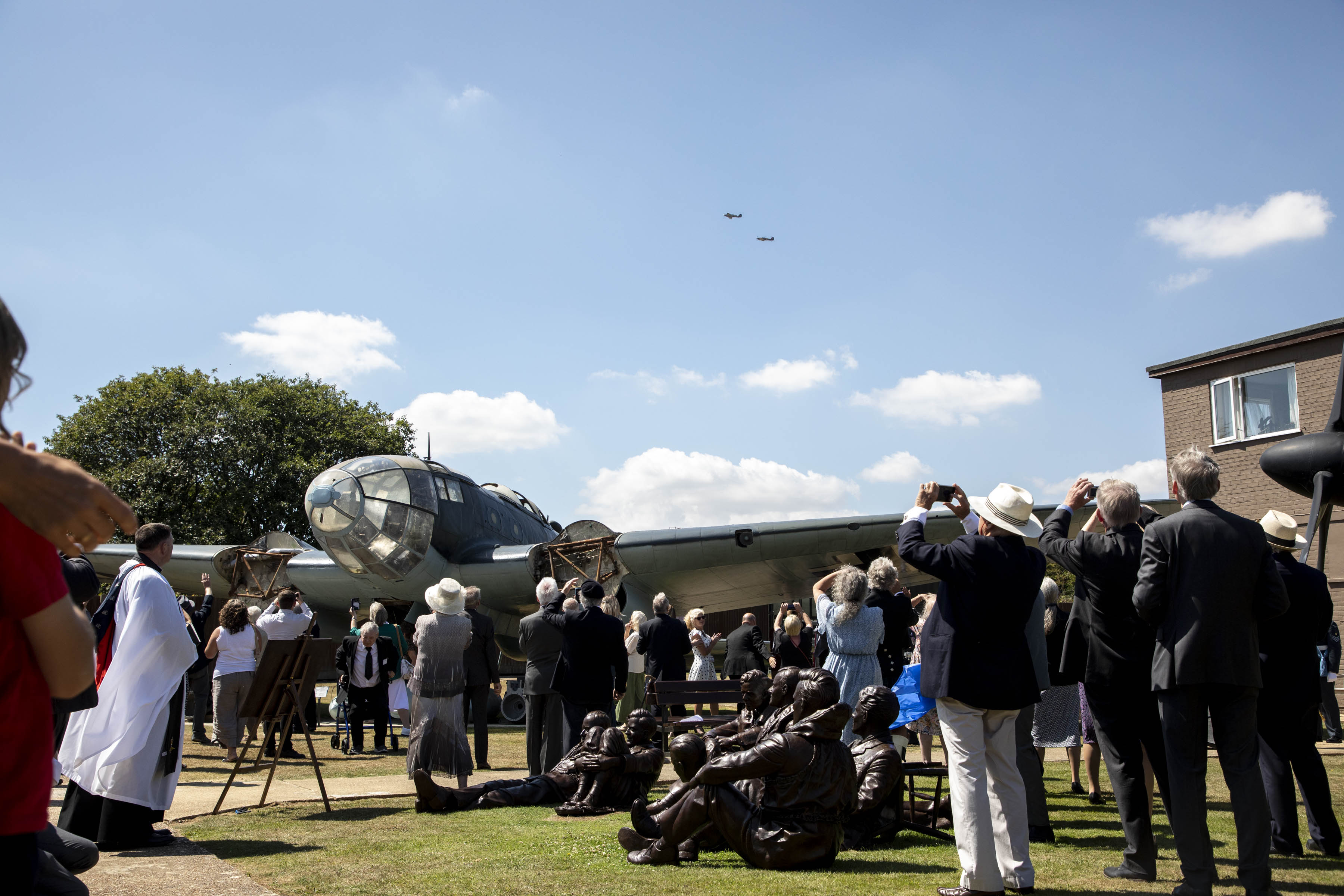 Image shows aviators and members of the public outside with Hurricane aircraft taking picture of flypast.