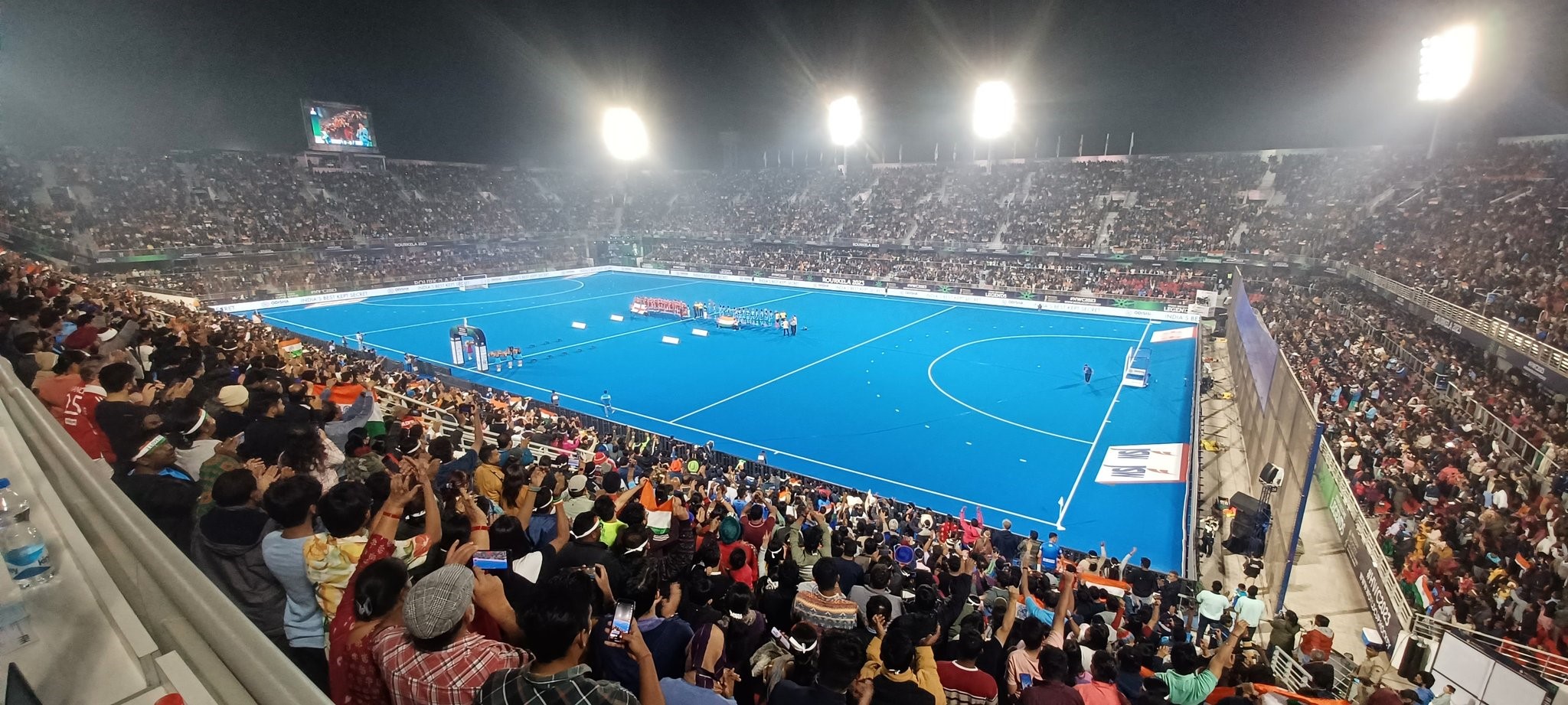 Image shows a view of an indoor hockey pitch from a full crowd viewing area.