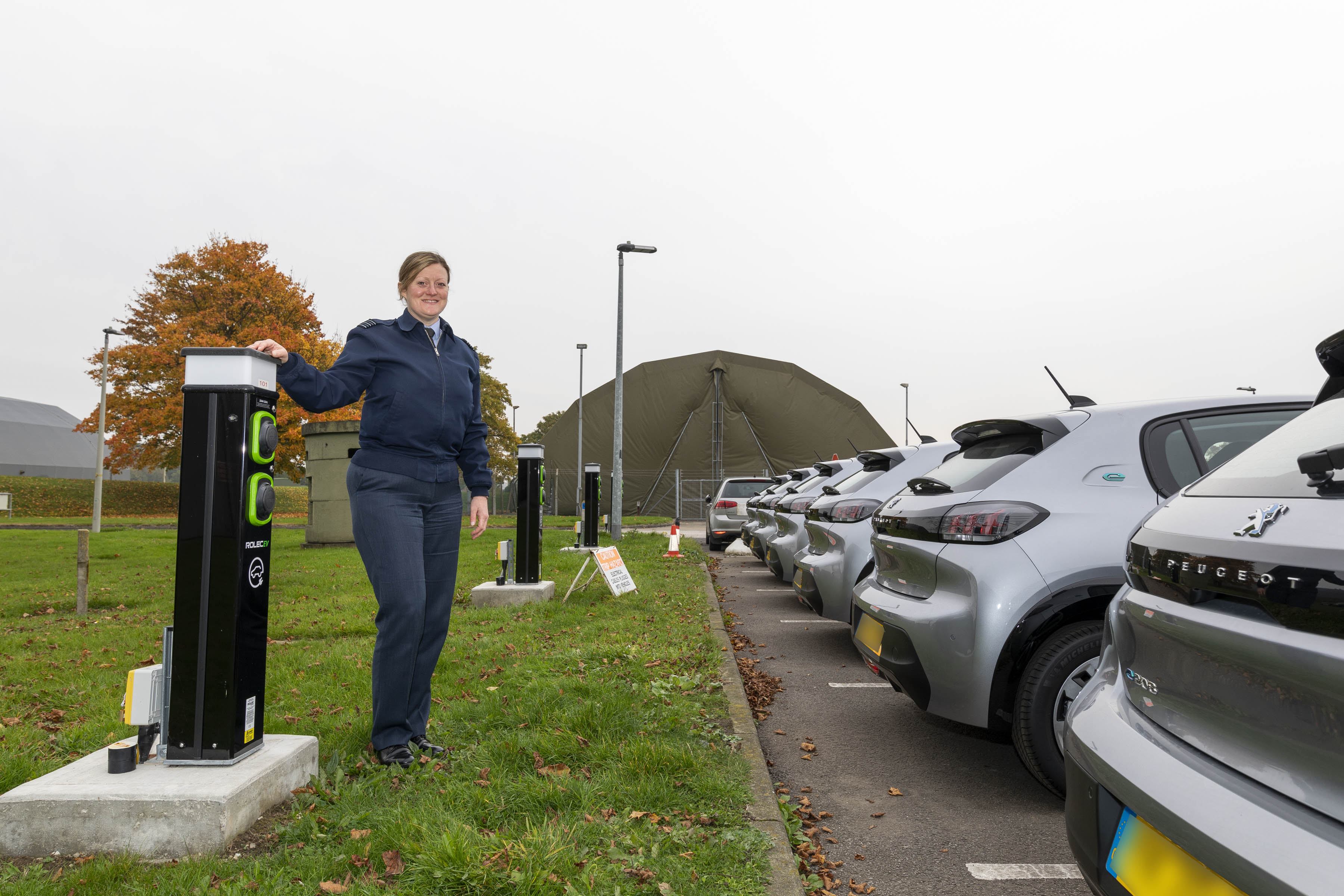 Image shows aviator standing by electric charging station in car park.