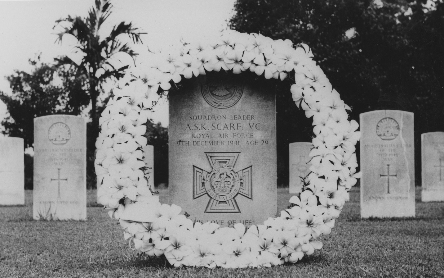 Black and white image shows Arthur Scarfs headstone with a wreath of flowers in the cemetery.